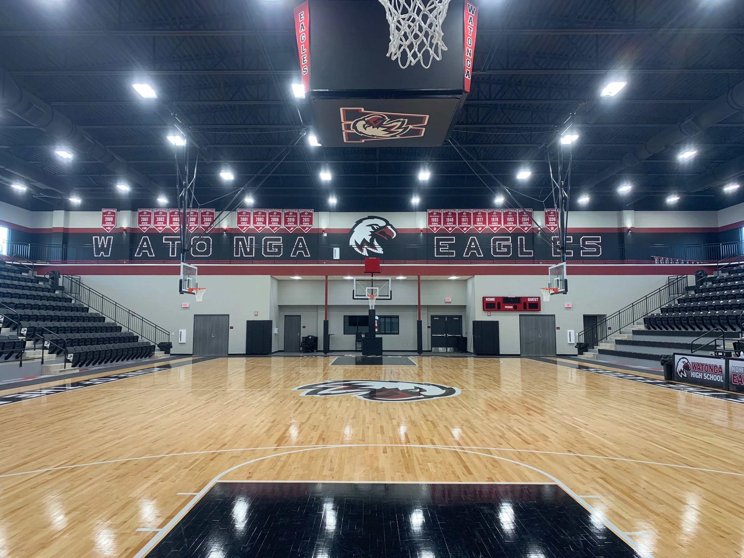 Empty indoor basketball court with Watonga Eagles signage, scoreboard, and banners hanging from the ceiling.