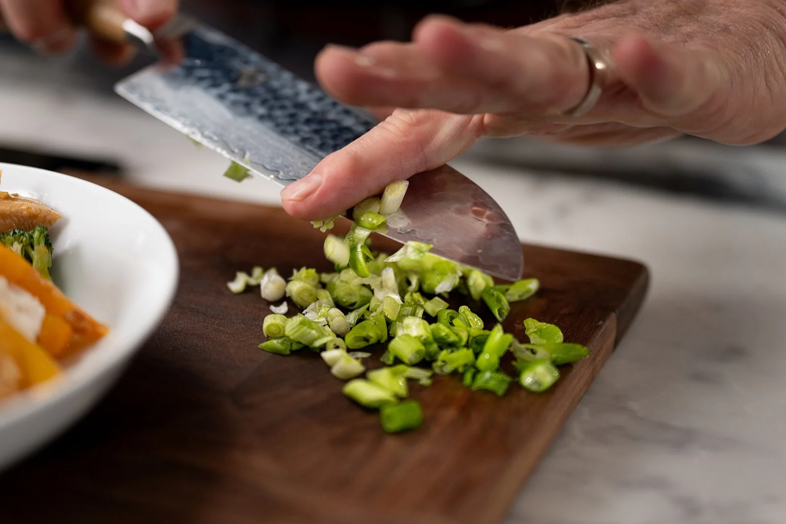 man's hand pushing chopped green onions off of knife edge onto cutting board