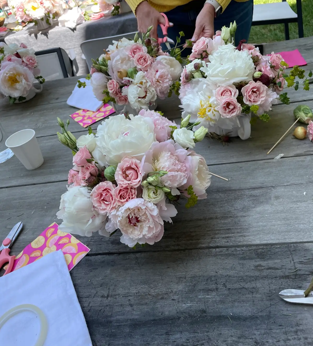 A person is arranging pink and white flower bouquets on a wooden table for a celebration or event.