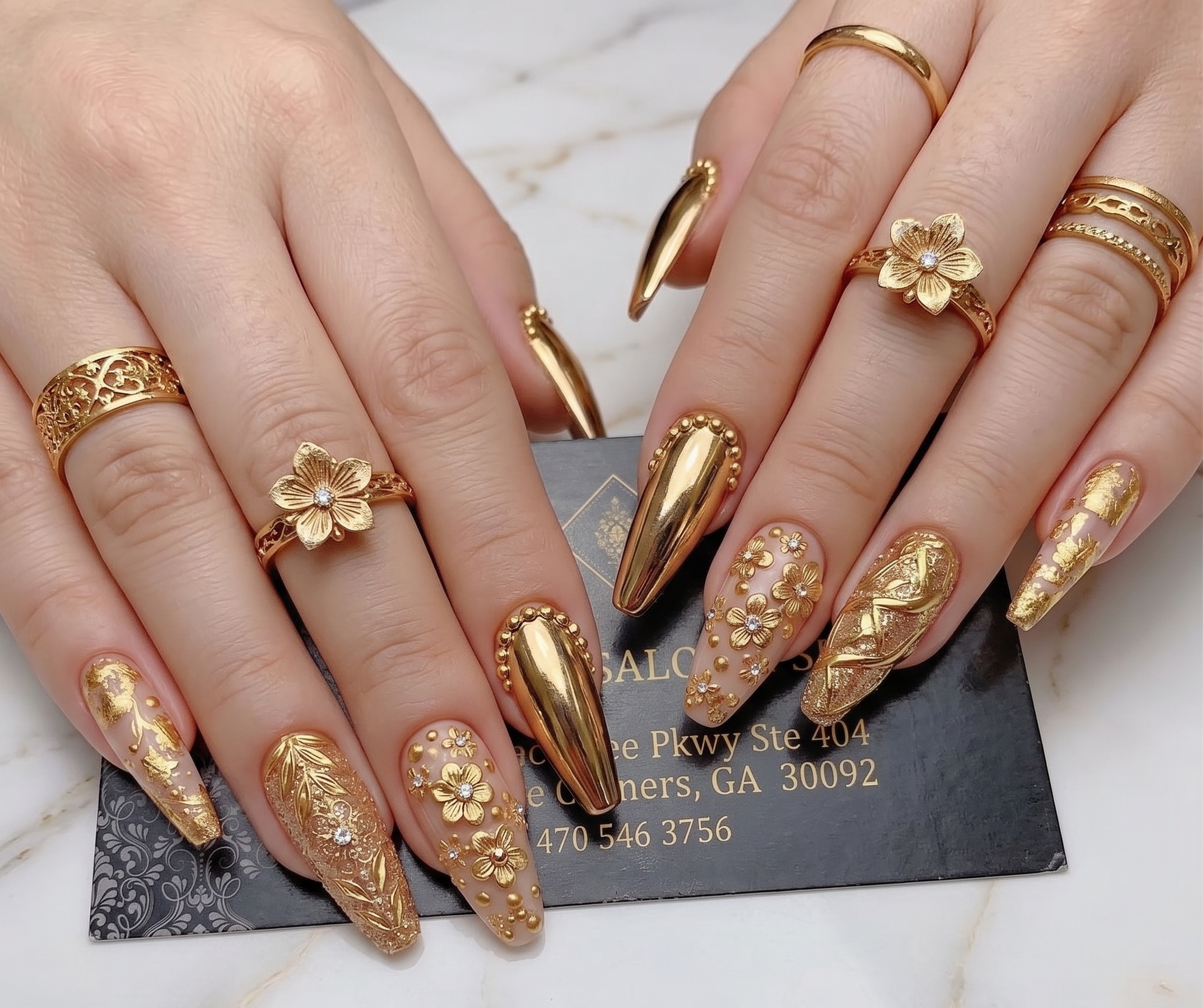 Close-up of ornate gold-and-nude floral nail art with rhinestones, surrounded by gold flower rings.