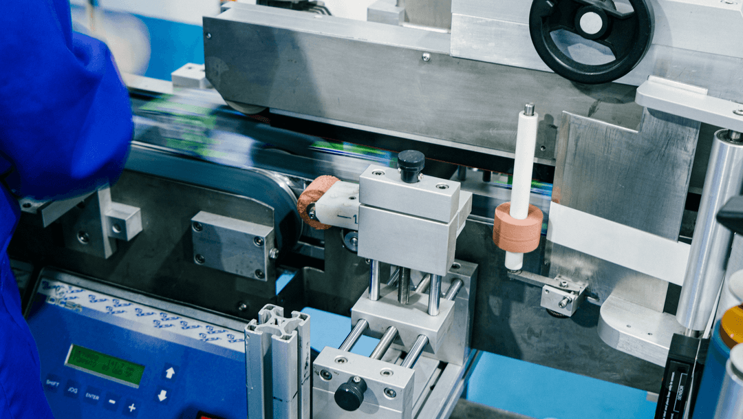 Close-up of industrial machinery in a manufacturing or packaging line, with a person wearing a blue uniform operating the equipment.