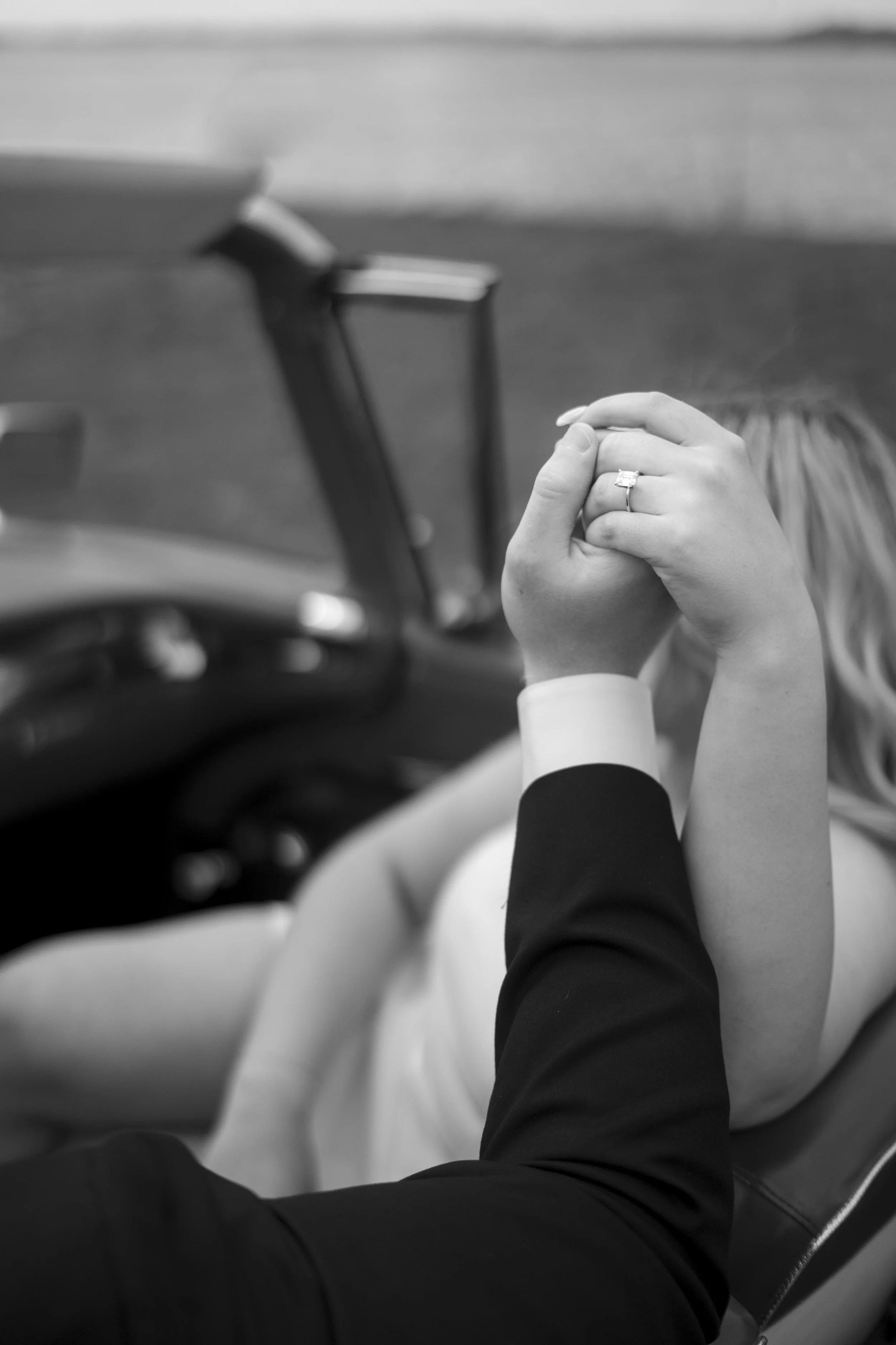 A close-up of a couple holding hands, with the woman wearing a wedding ring, inside a car.