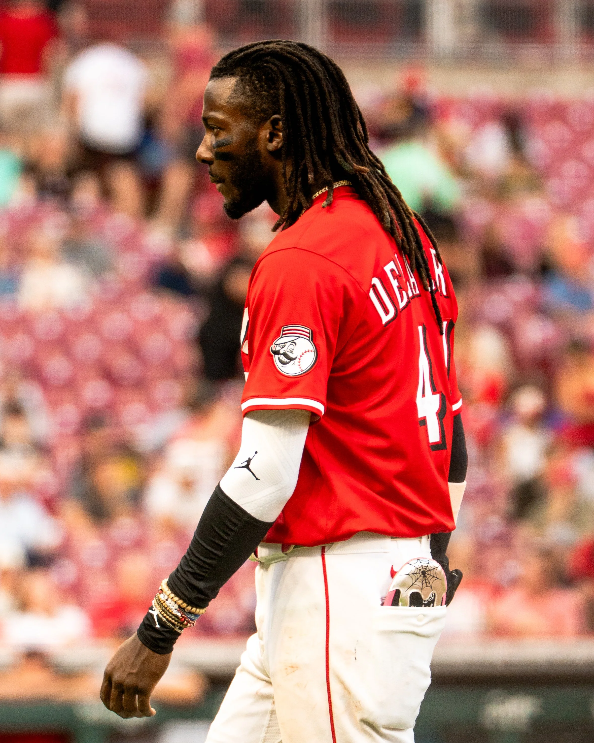 A baseball player with long dreadlocks wearing a red jersey with the name Devers and the number 11 on the back, standing on the field during a game, with a crowd in the background.