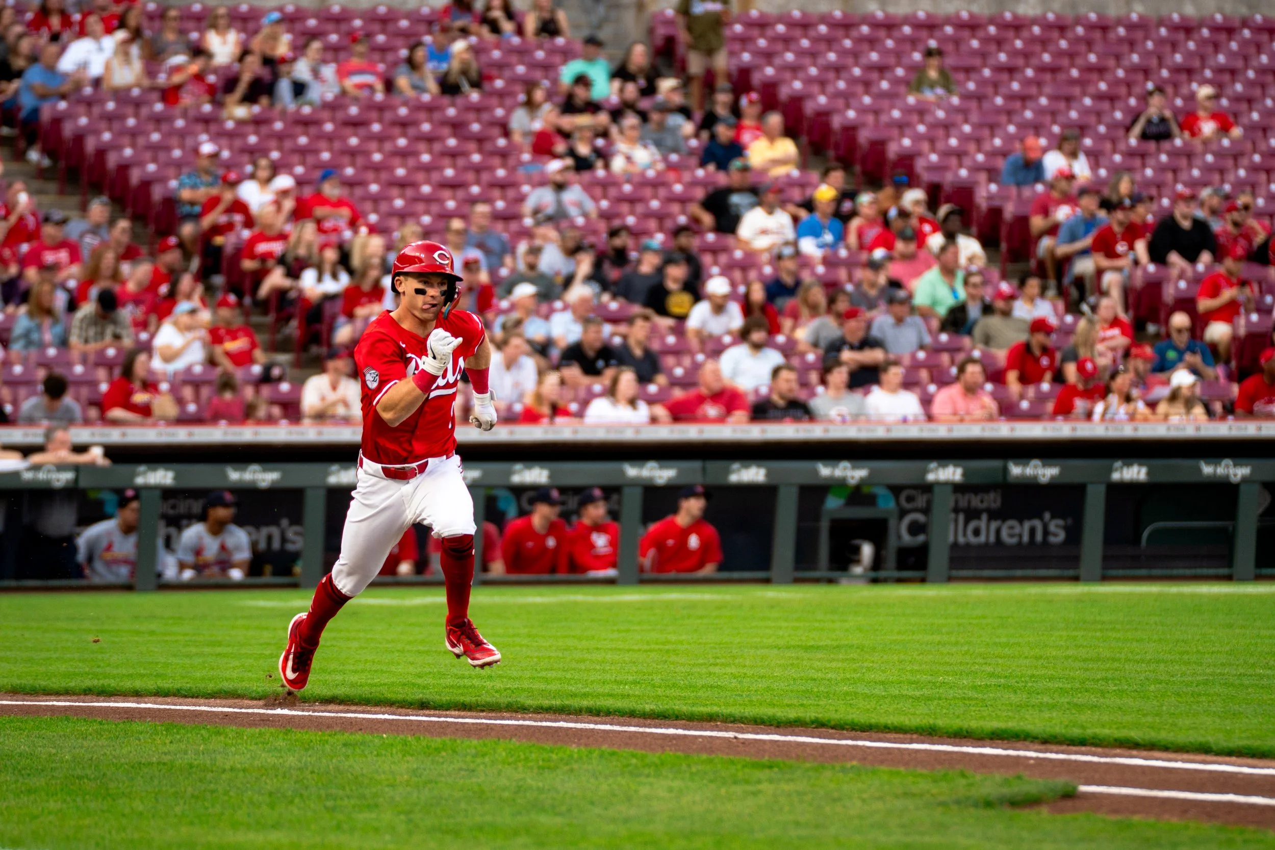 A baseball player in a red uniform running on the field during a game in a stadium filled with spectators.