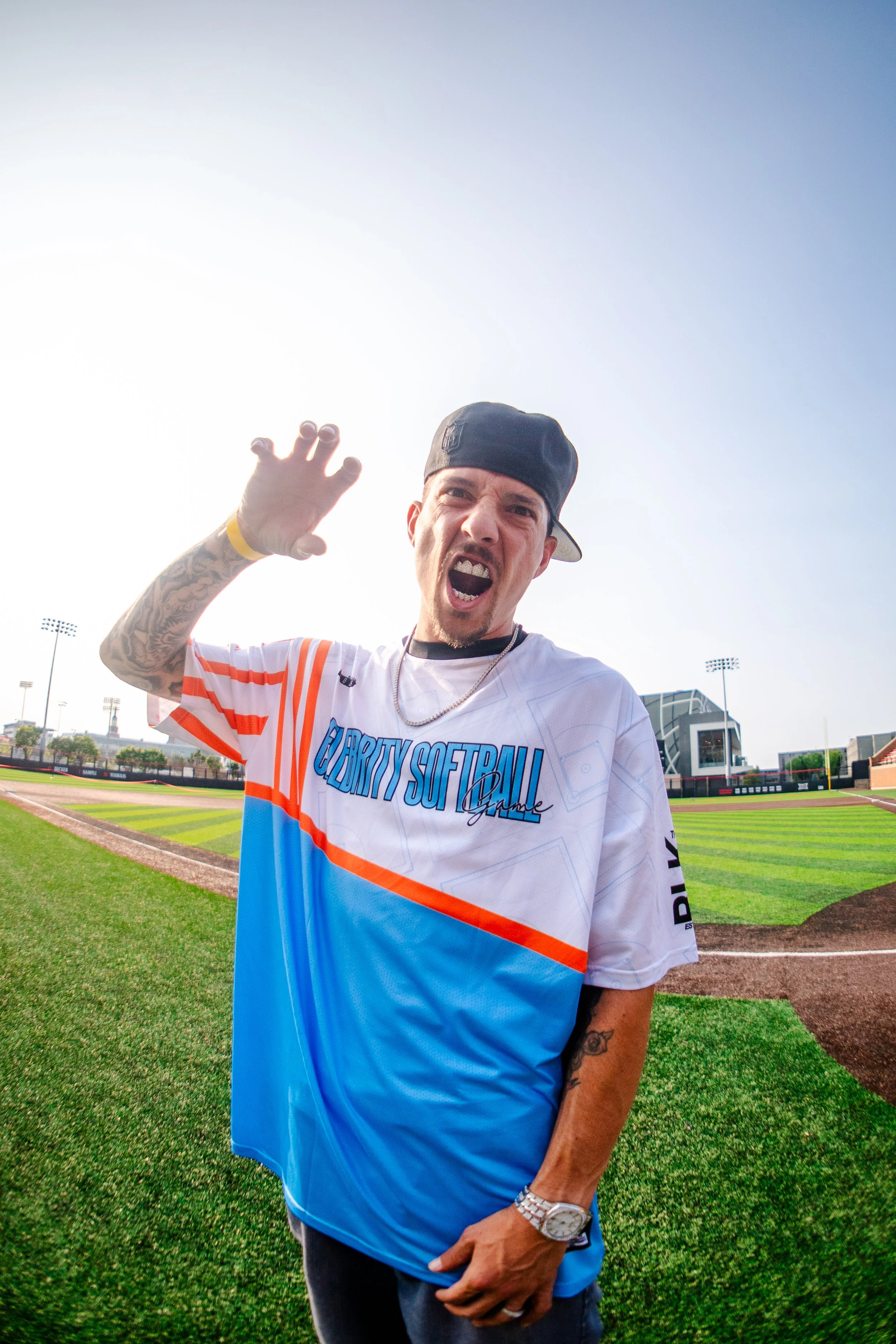 A man at a baseball field, wearing a custom sports jersey, making an expressive face and gesture