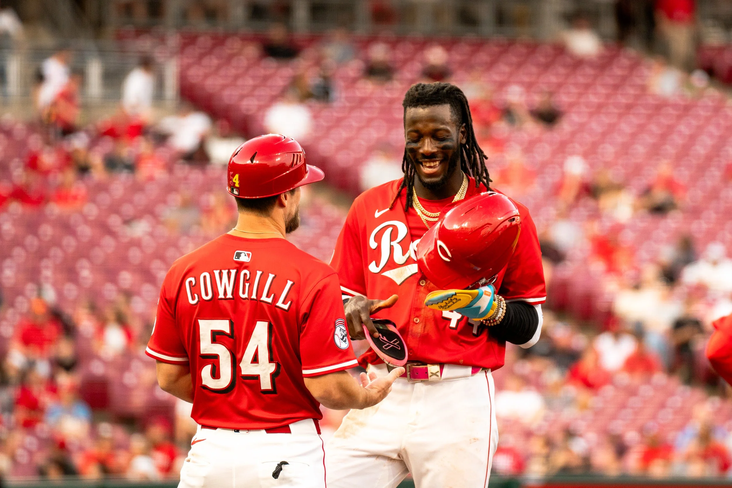 Two baseball players in red and white uniforms celebrating on the field. One player has the name 'COWGILL' and number 54 on the back, and the other has the letters 'R' on the front of his jersey. They are smiling and talking, with one holding a red h
