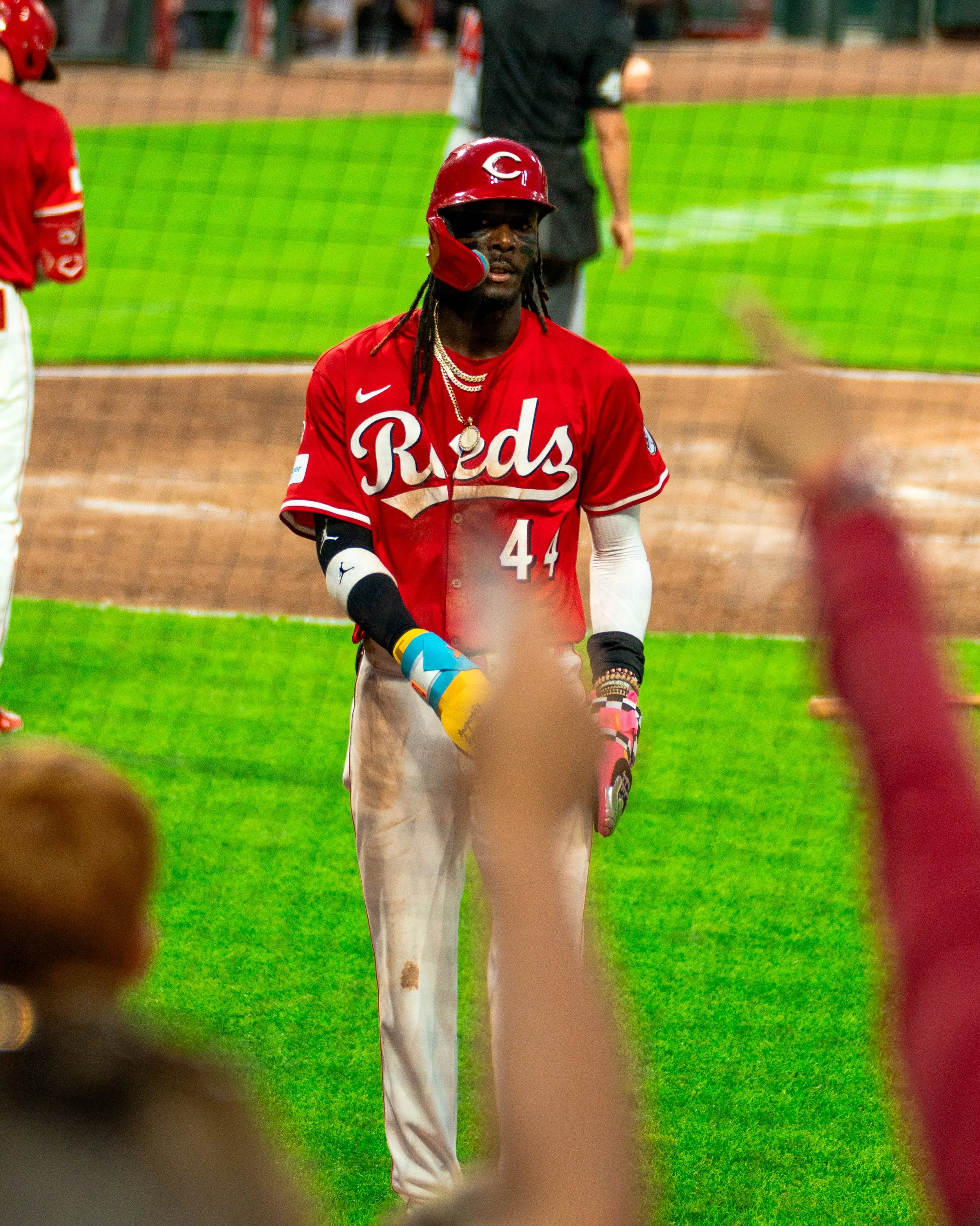 A baseball player from the Cincinnati Reds standing on the field during a game, wearing a red jersey, helmet, and gloves.