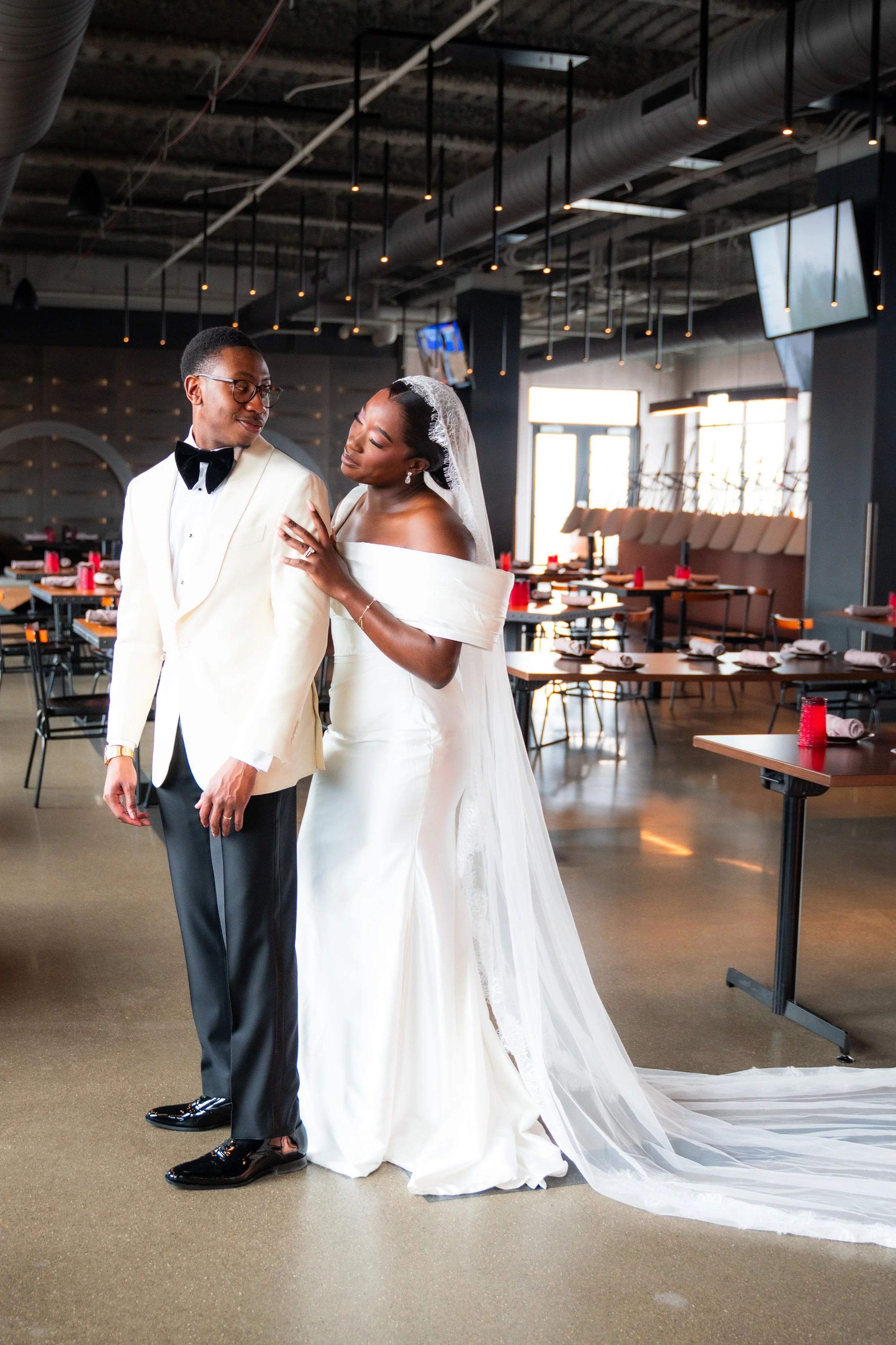 Bride and groom on their wedding day in a modern, industrial-style venue with tables set for celebration.