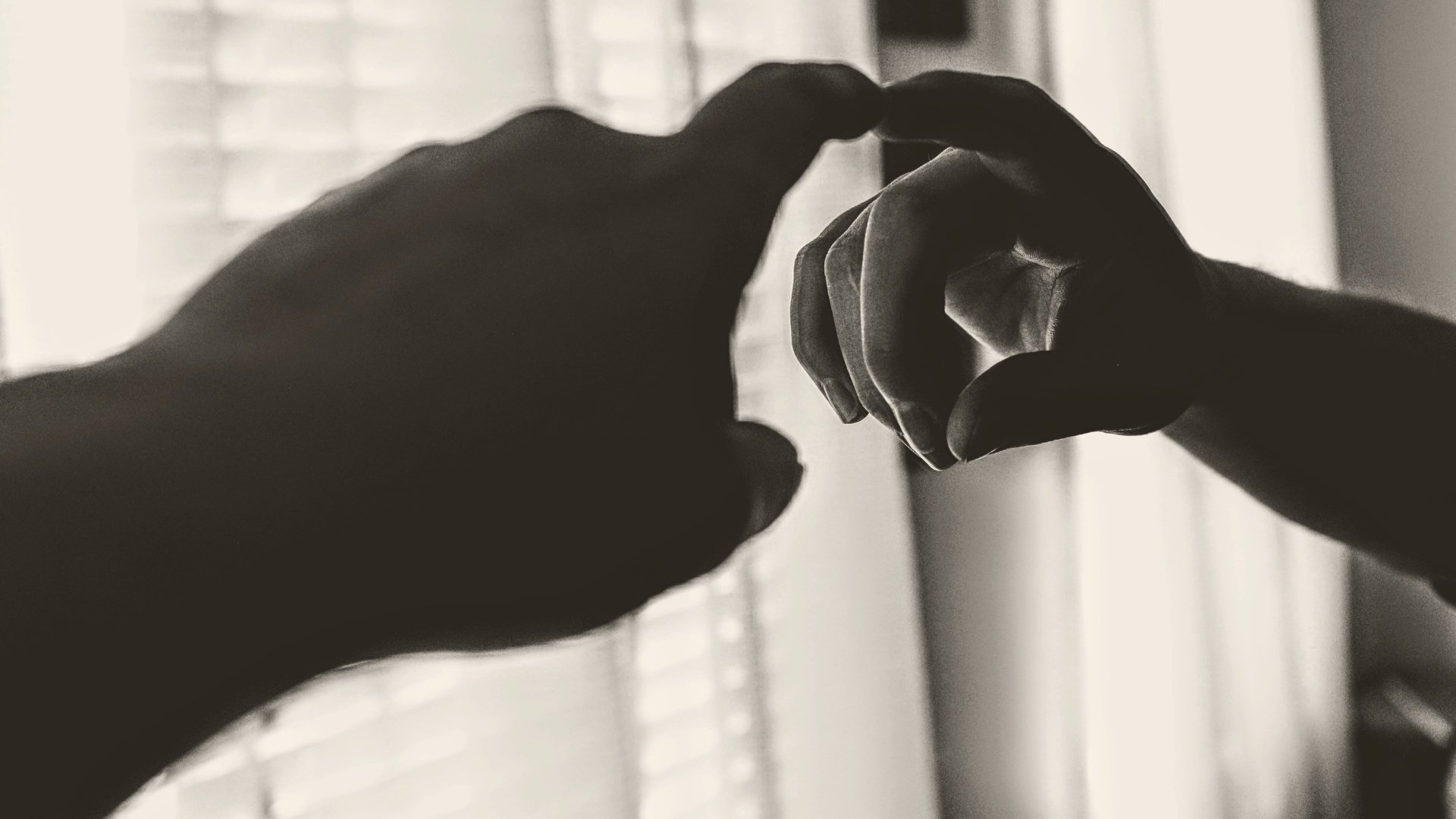 Black and white photo of a finger touching its reflection in the mirror, with a window in the background.