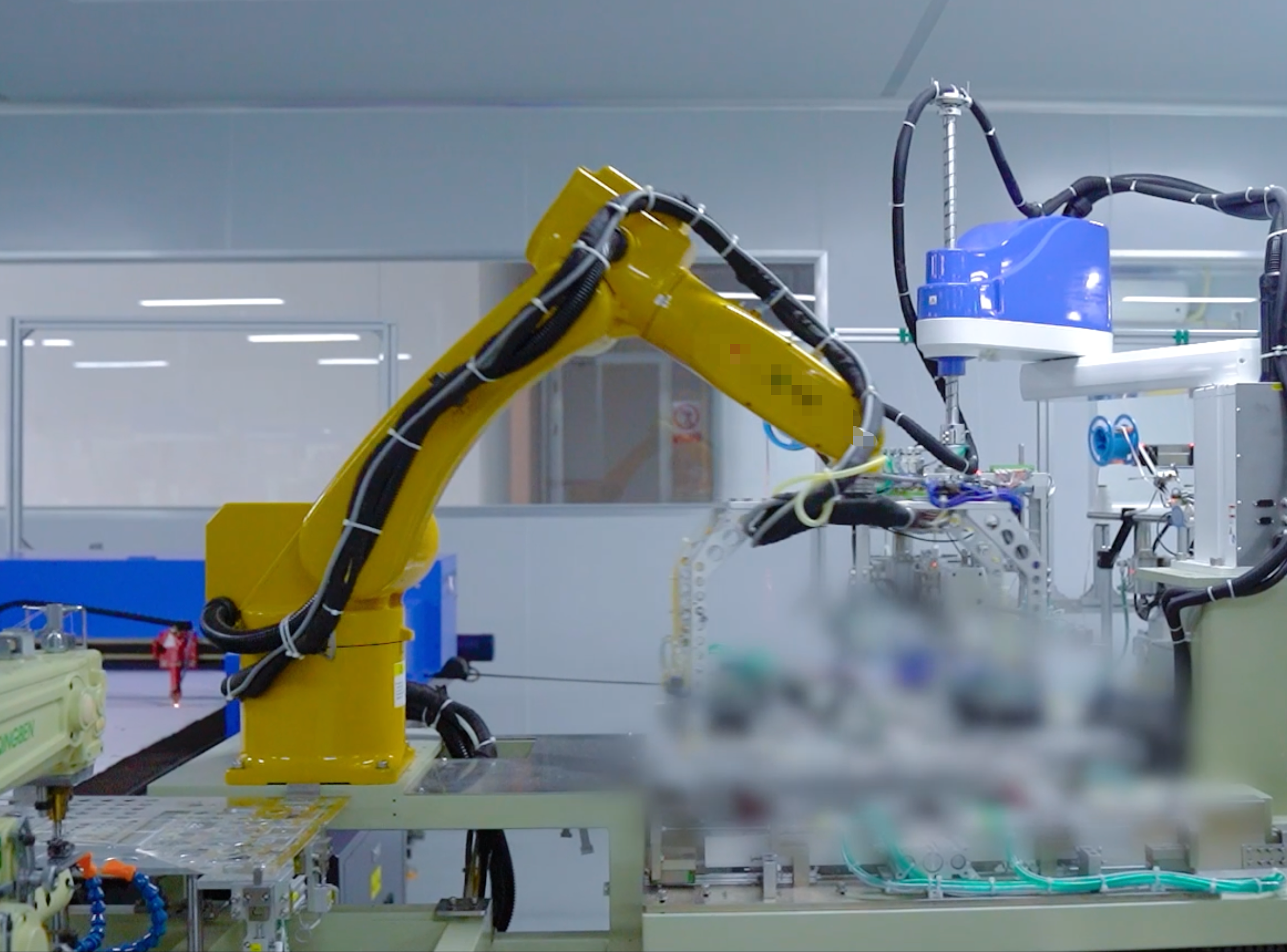 A yellow robotic arm working on electronic components on a workbench in a high-tech laboratory.