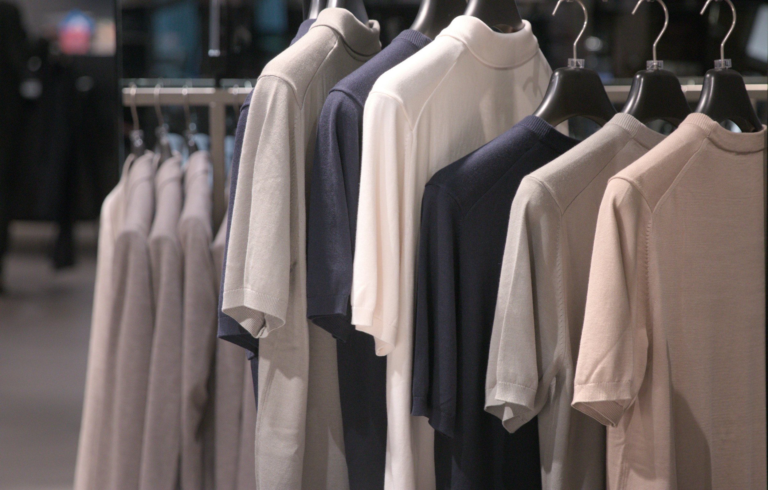 A row of sweatshirts hanging on black hangers, with colors including beige, navy, white, and gray, displayed in a retail store.