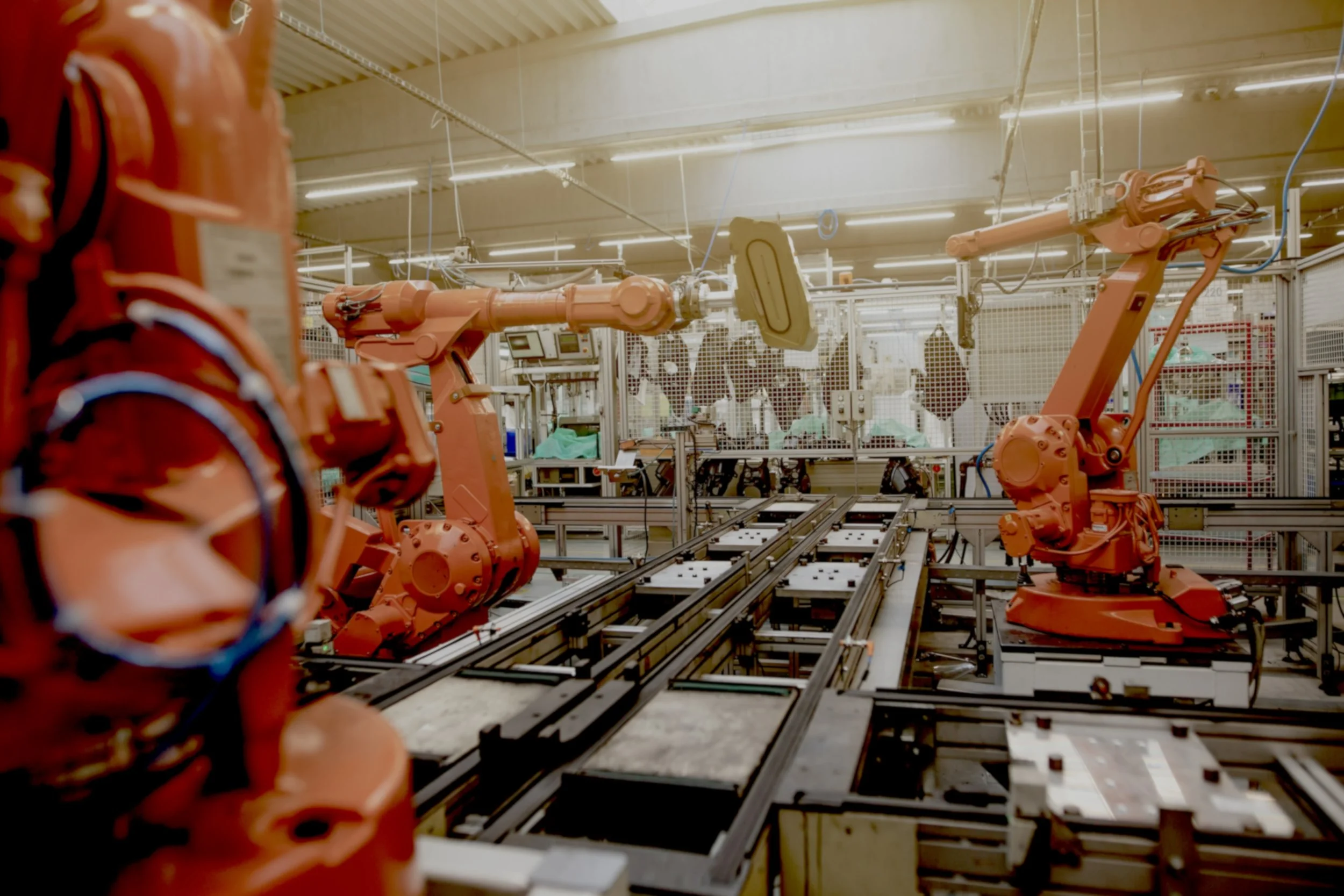 Factory or industrial setting with multiple orange robotic arms working on assembly lines.