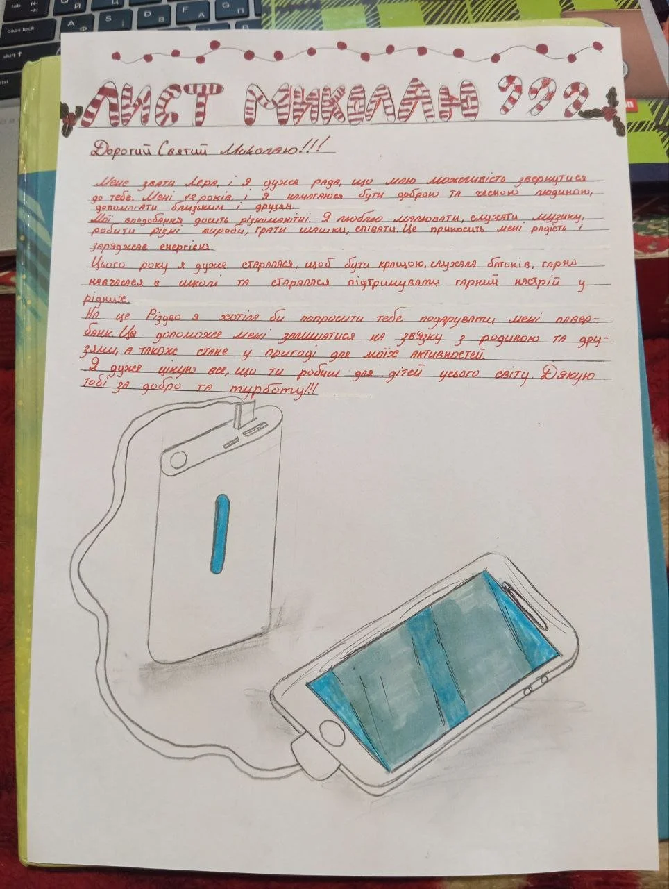 A handwritten letter in Ukrainian with red and black ink, decorated with Christmas-themed illustrations including candy canes and Christmas lights at the top. The letter includes a drawing of a portable power bank connected to a smartphone via a char