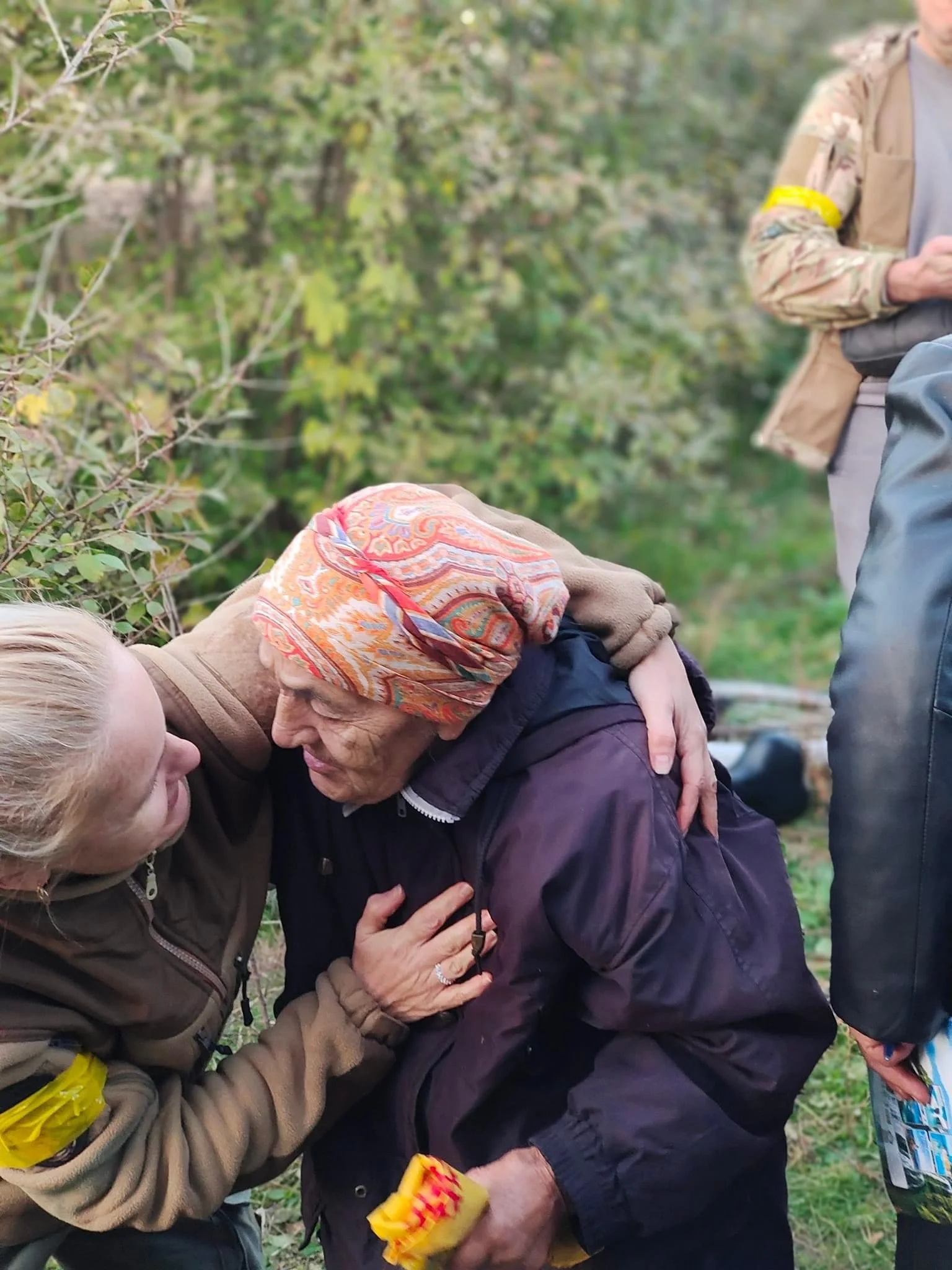 A young woman comfortingly holding an elderly woman during a moment of emotional distress outdoors.