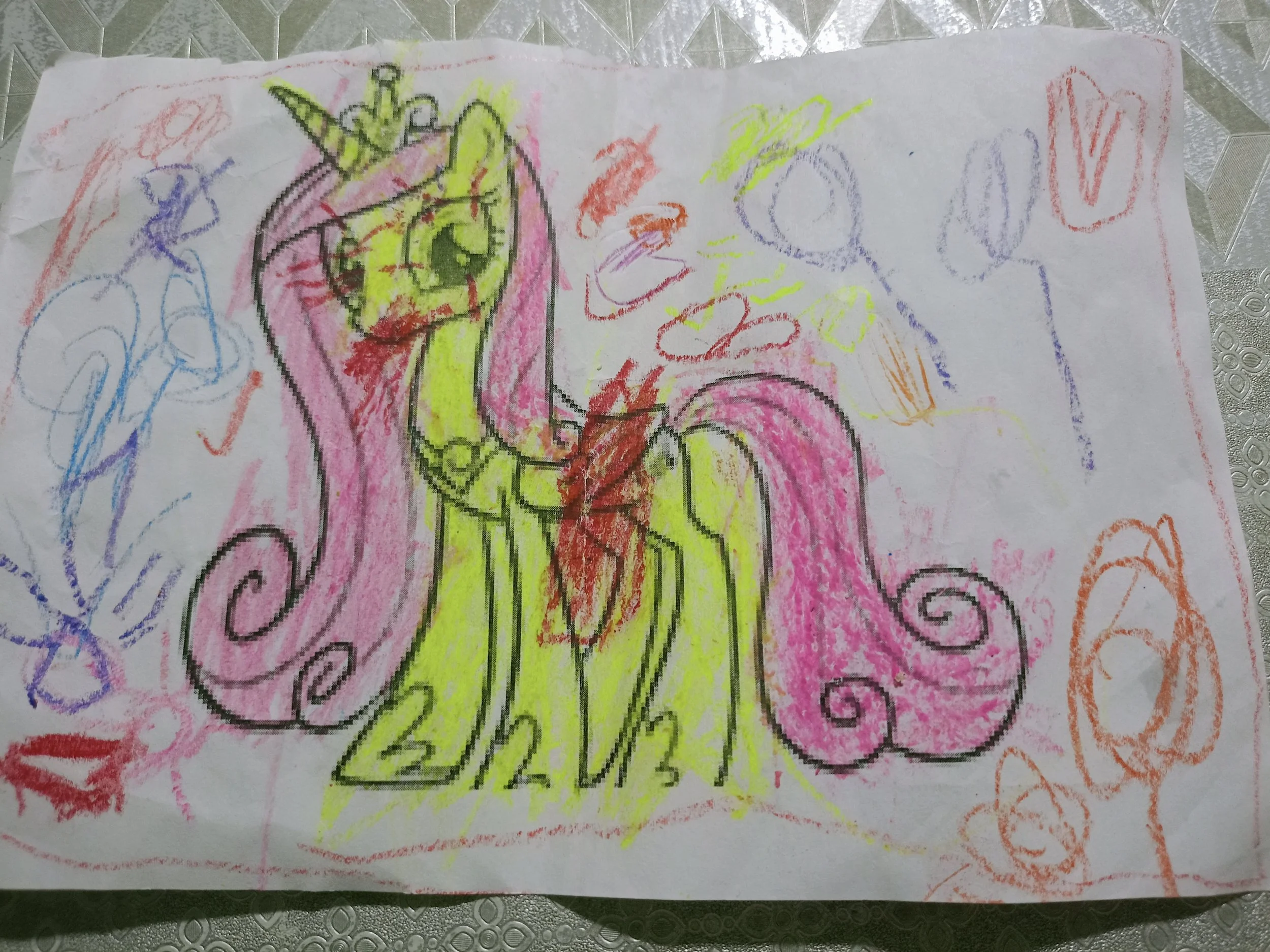 Child's drawing of a colorful unicorn with pink and yellow body, purple and pink mane, and a yellow horn, surrounded by various scribbles and shapes in different colors.
