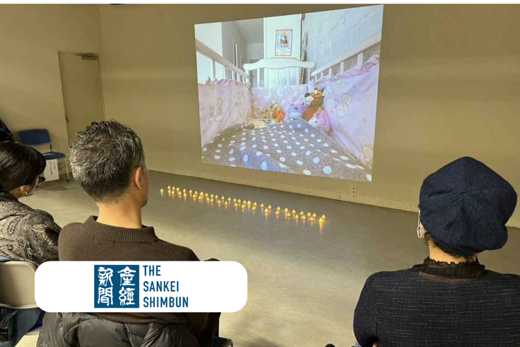 People sitting in a room watching a video projection of a child's bedroom with stuffed animals on a bed.
