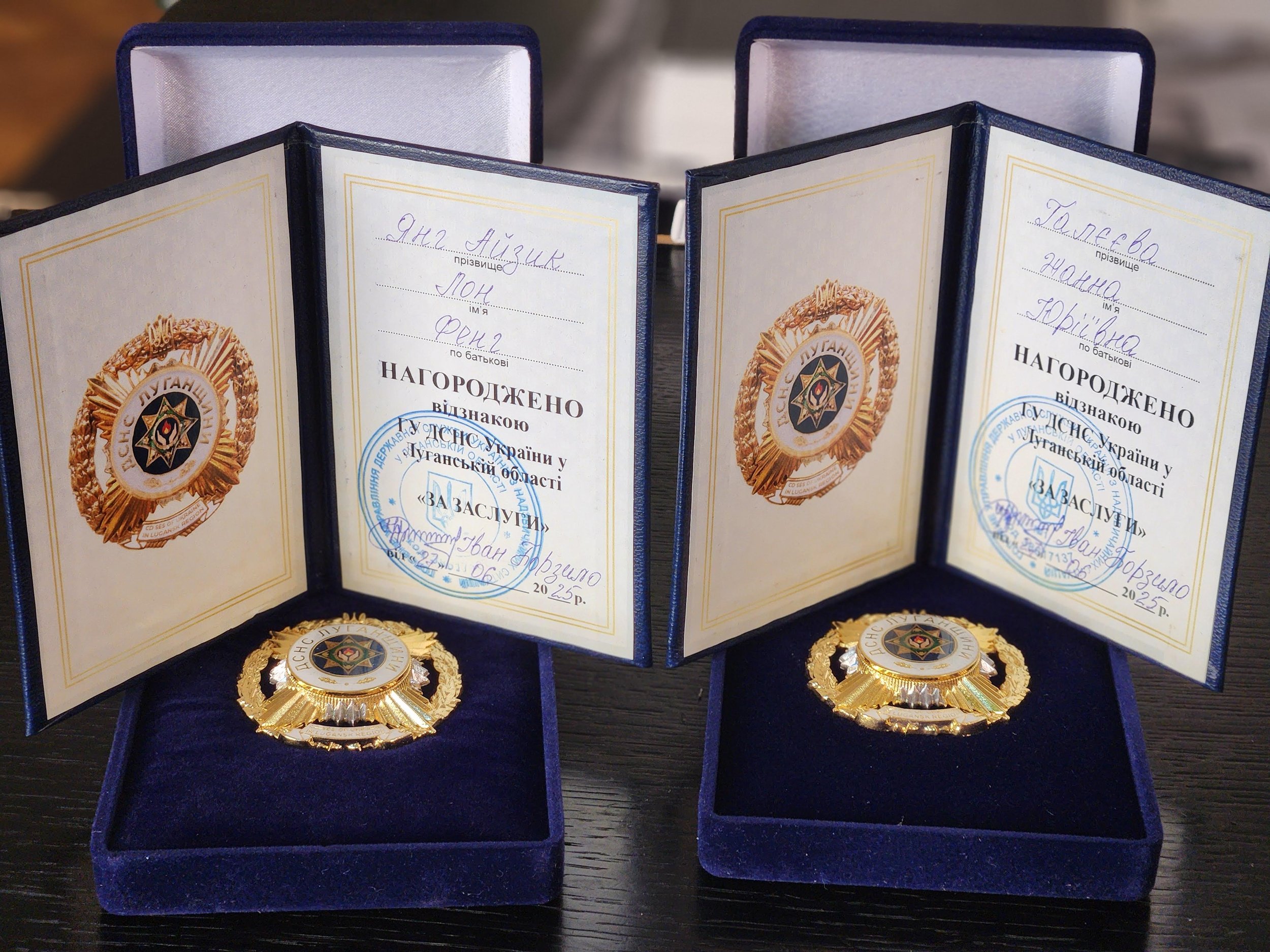 Two open navy blue presentation boxes each containing a Ukrainian police medal and an official certificate inside. The certificates have handwriting in Ukrainian and official stamps.