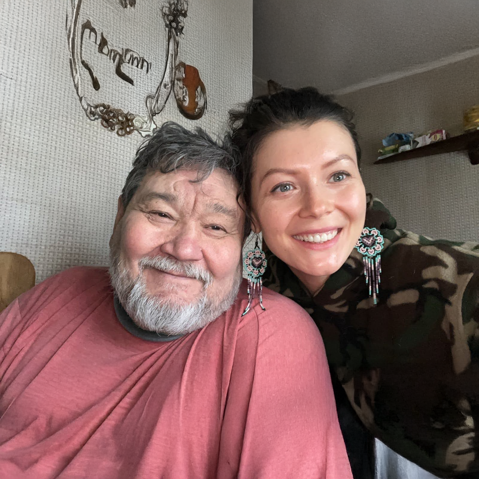 A smiling man with a gray beard and a woman with long dark hair taking a selfie together indoors.