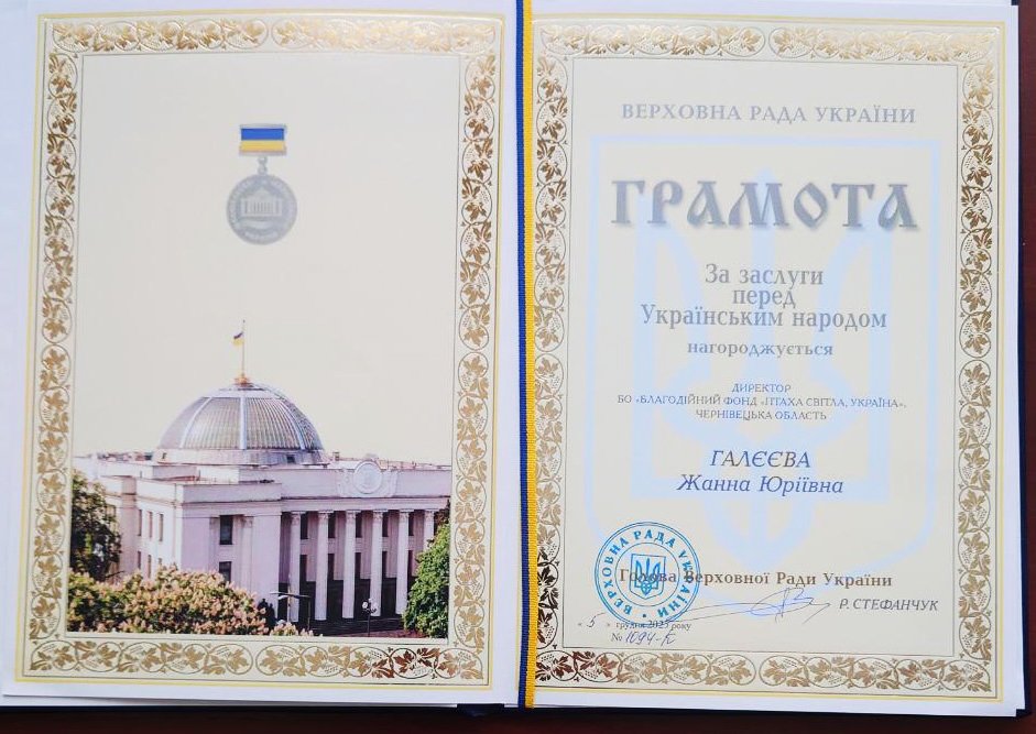 Open Ukrainian certificate featuring a photograph of a government building with a dome, a flag, and a medallion with a blue and yellow ribbon, indicating recognition or award from the Ukrainian parliament, with ornate border decorations.