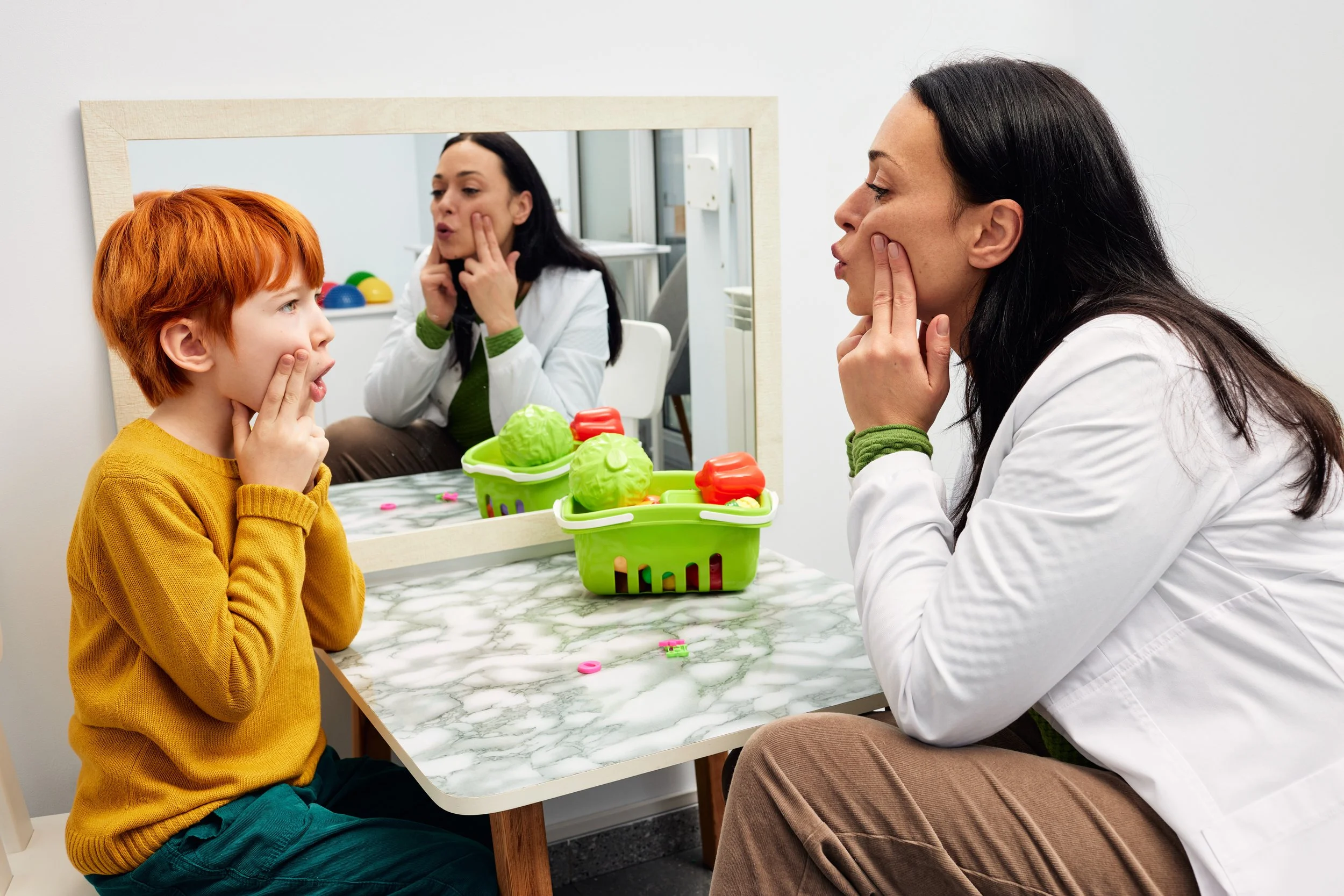A young boy with red hair practices his speech therapy with his Speech Language Pathologist.
