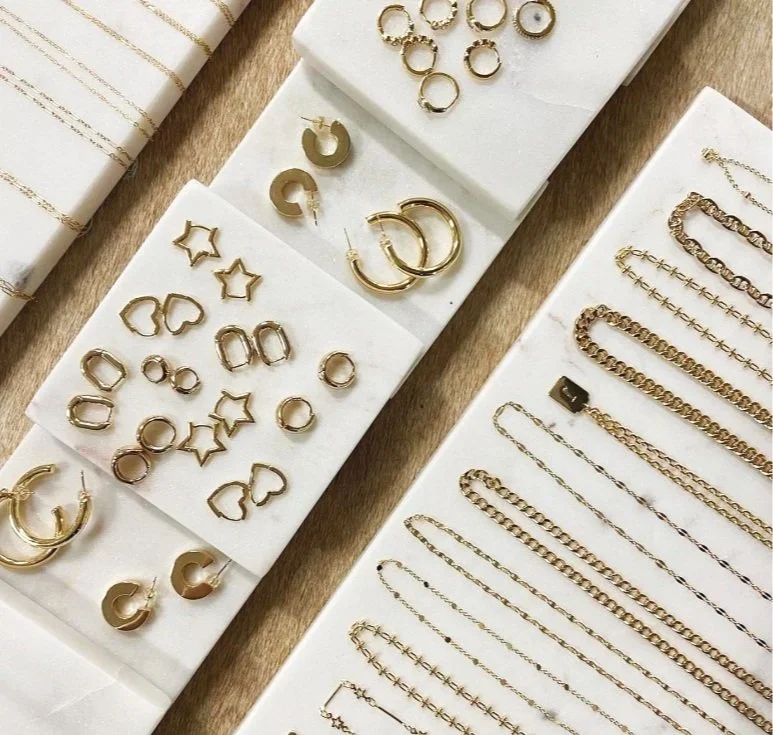 Display of various gold jewelry including earrings, rings, and chains arranged on white cards.