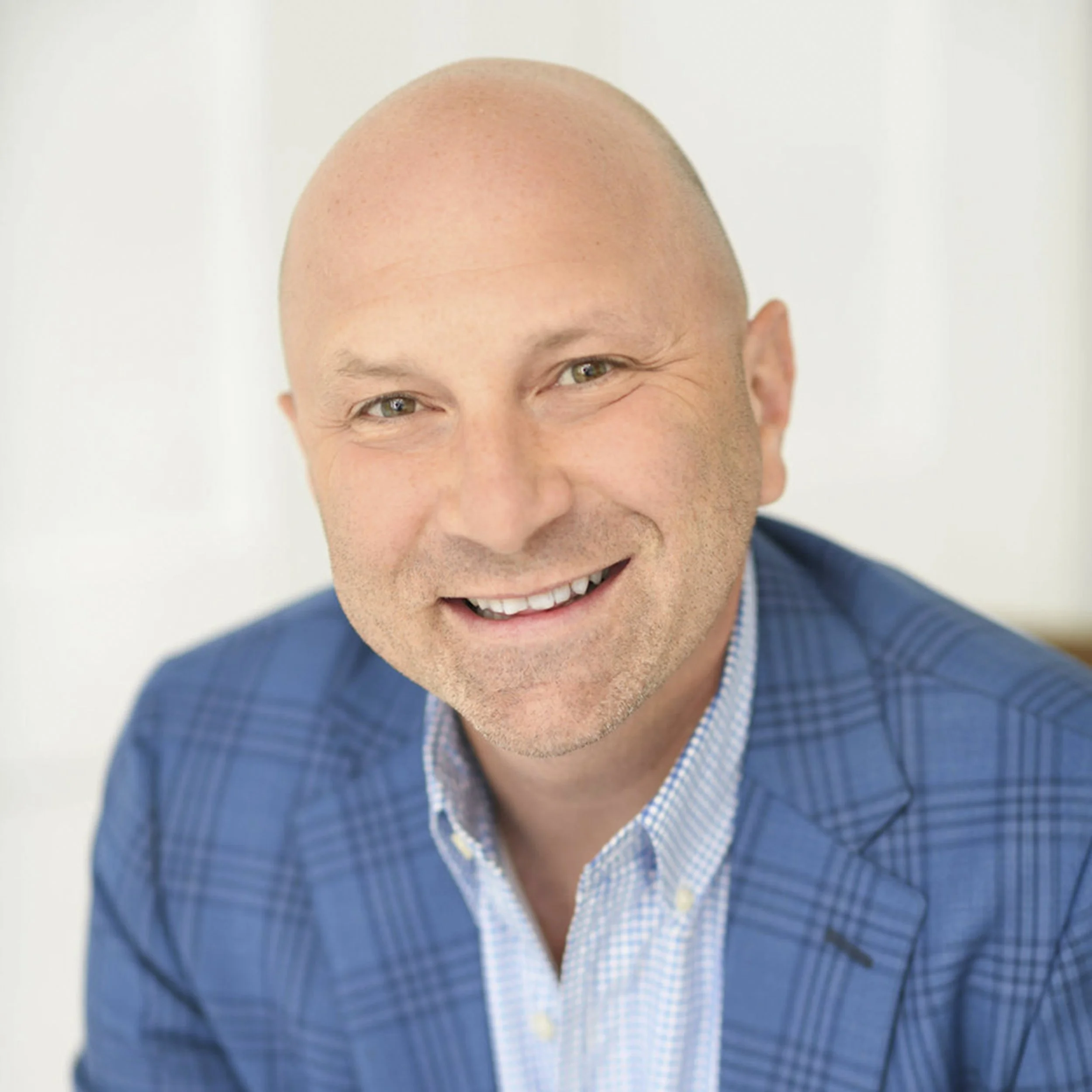 Headshot of a smiling bald man wearing a blue suit jacket and a light blue checkered shirt.