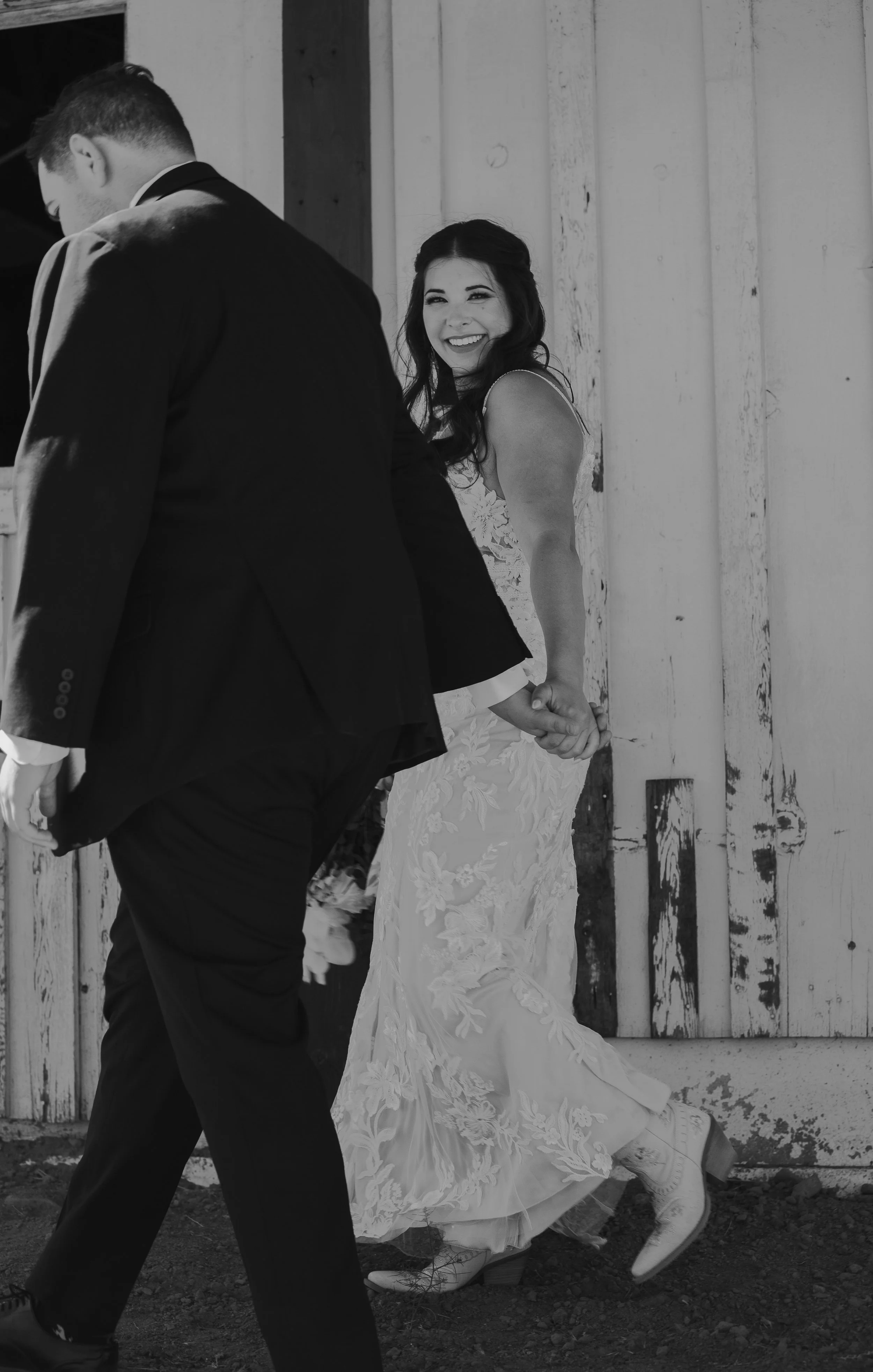 Black and white wedding portrait of the groom beside a weathered ranch building.