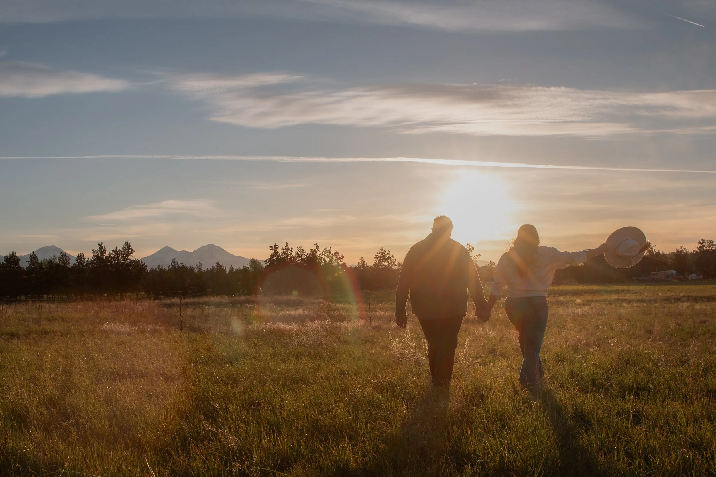 Wide sunset engagement portrait overlooking the open ranch landscape and Cascade Mountains near Bend, Oregon.