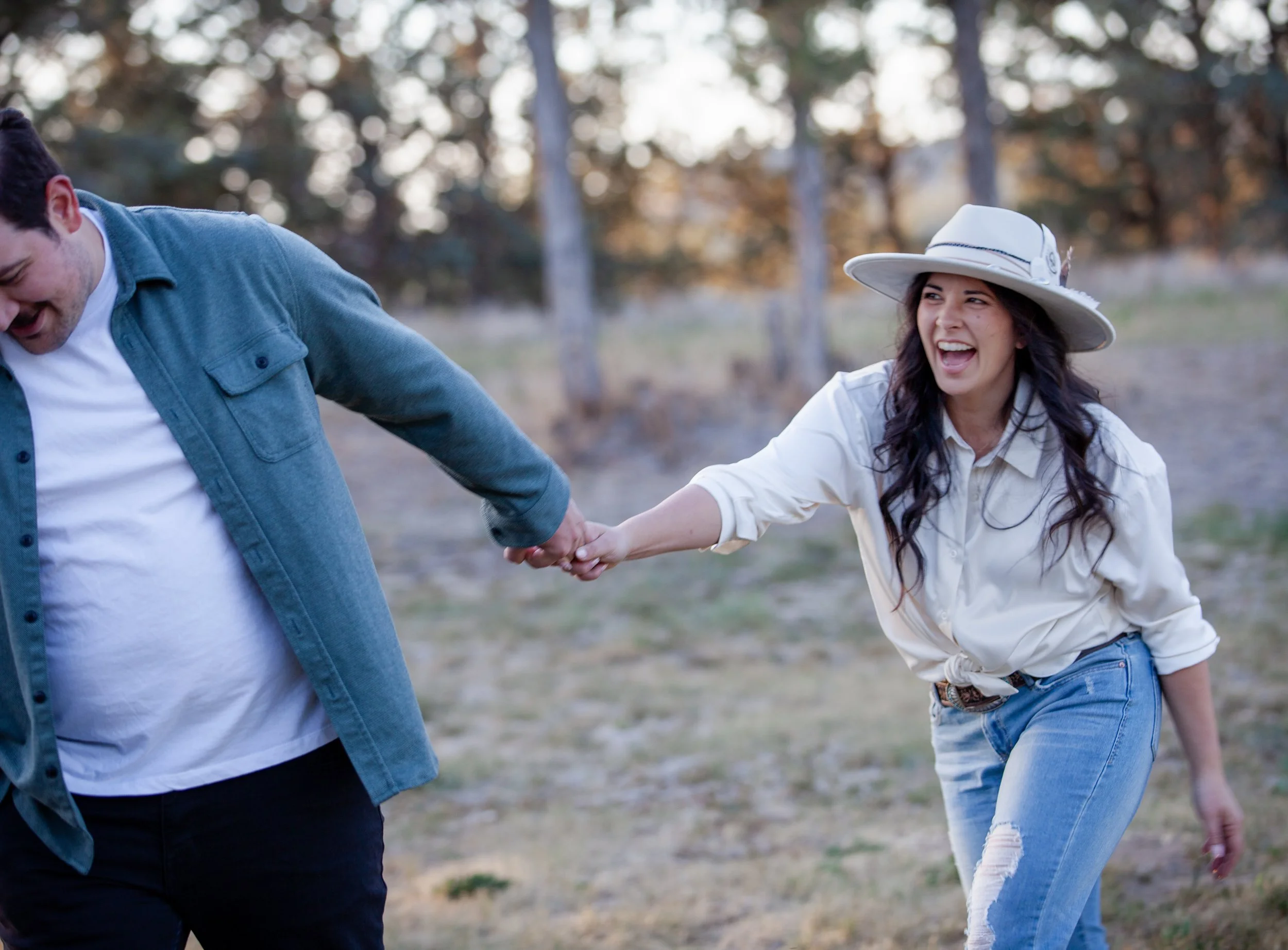Playful Western engagement portrait of a couple laughing together beneath the pines near Bend, Oregon.