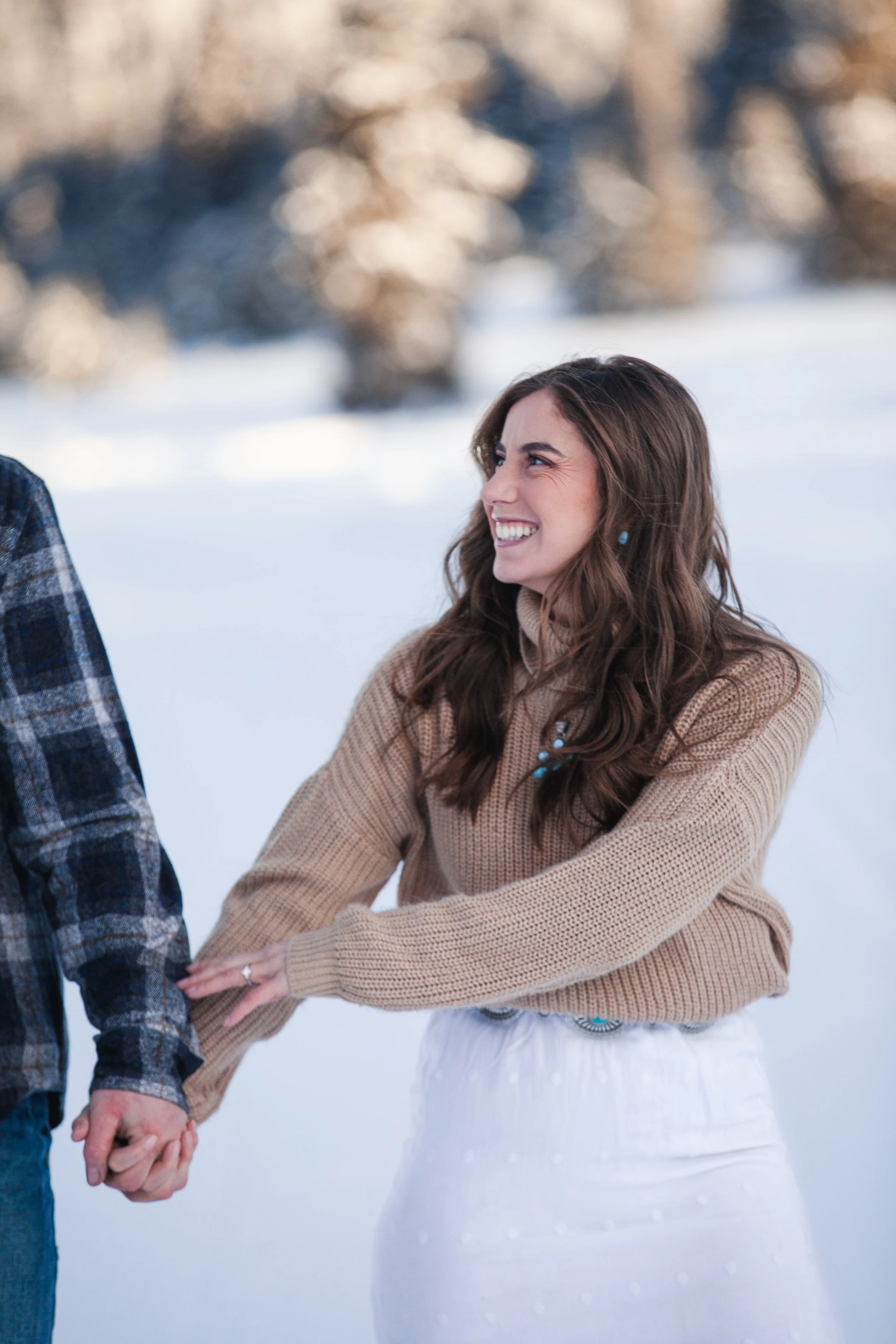 Close-up engagement portrait of a bride-to-be showing her ring while embracing her fiancé in the snow.