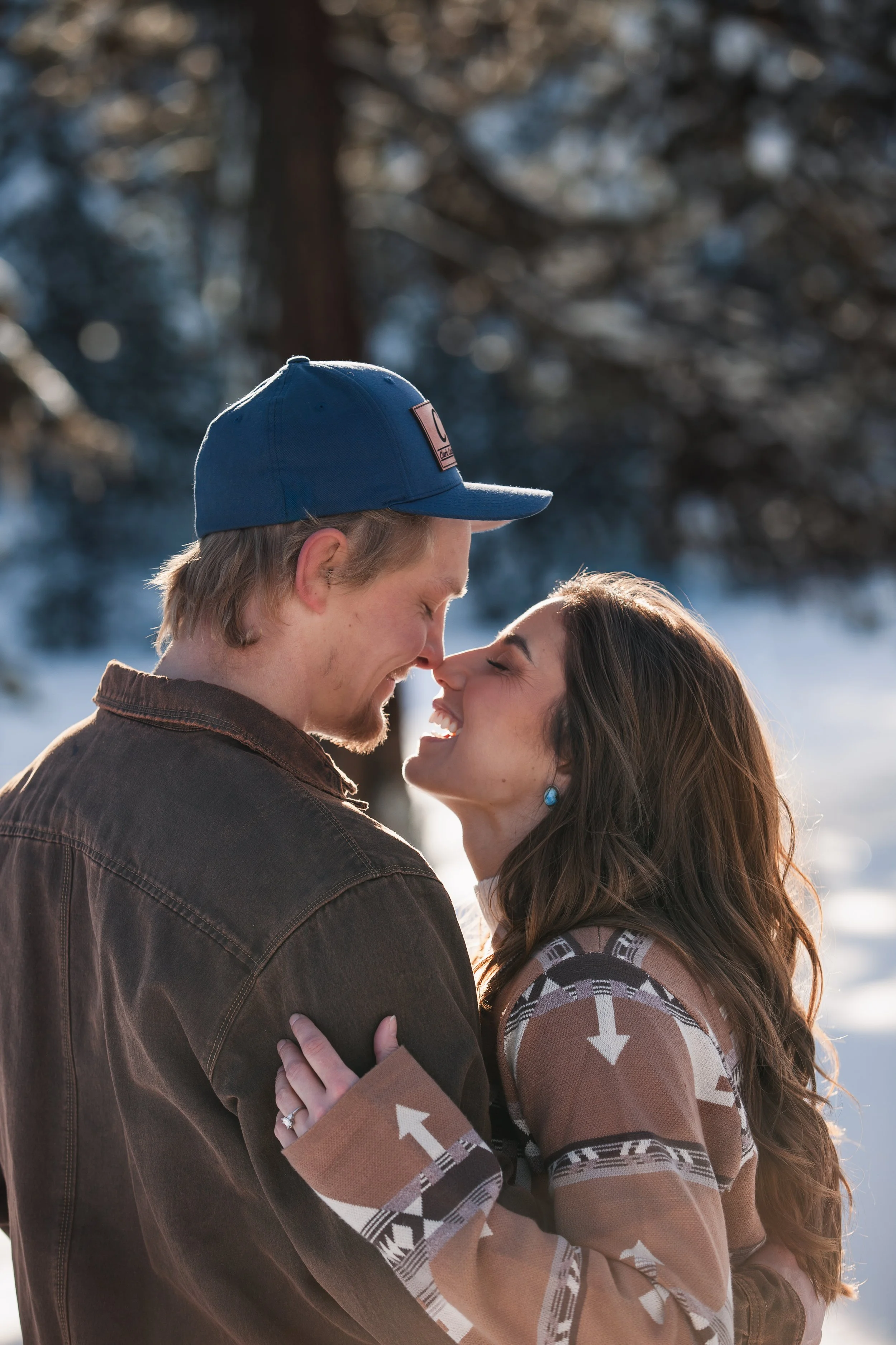 Engaged couple embracing on a snow-covered forest road during their Idaho winter engagement session.