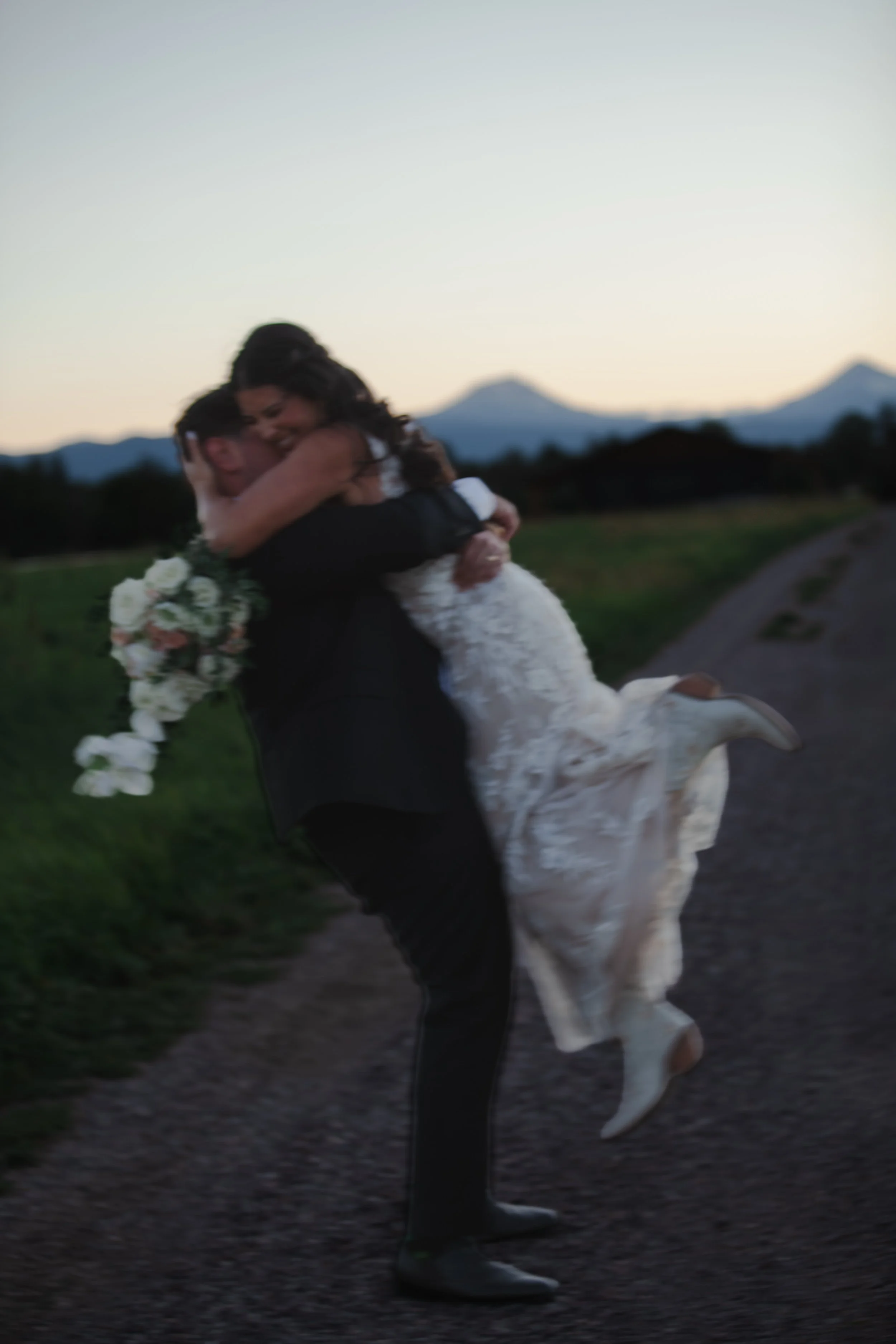  Newlyweds embracing on a ranch road with the Three Sisters mountains behind them near Bend, Oregon 
