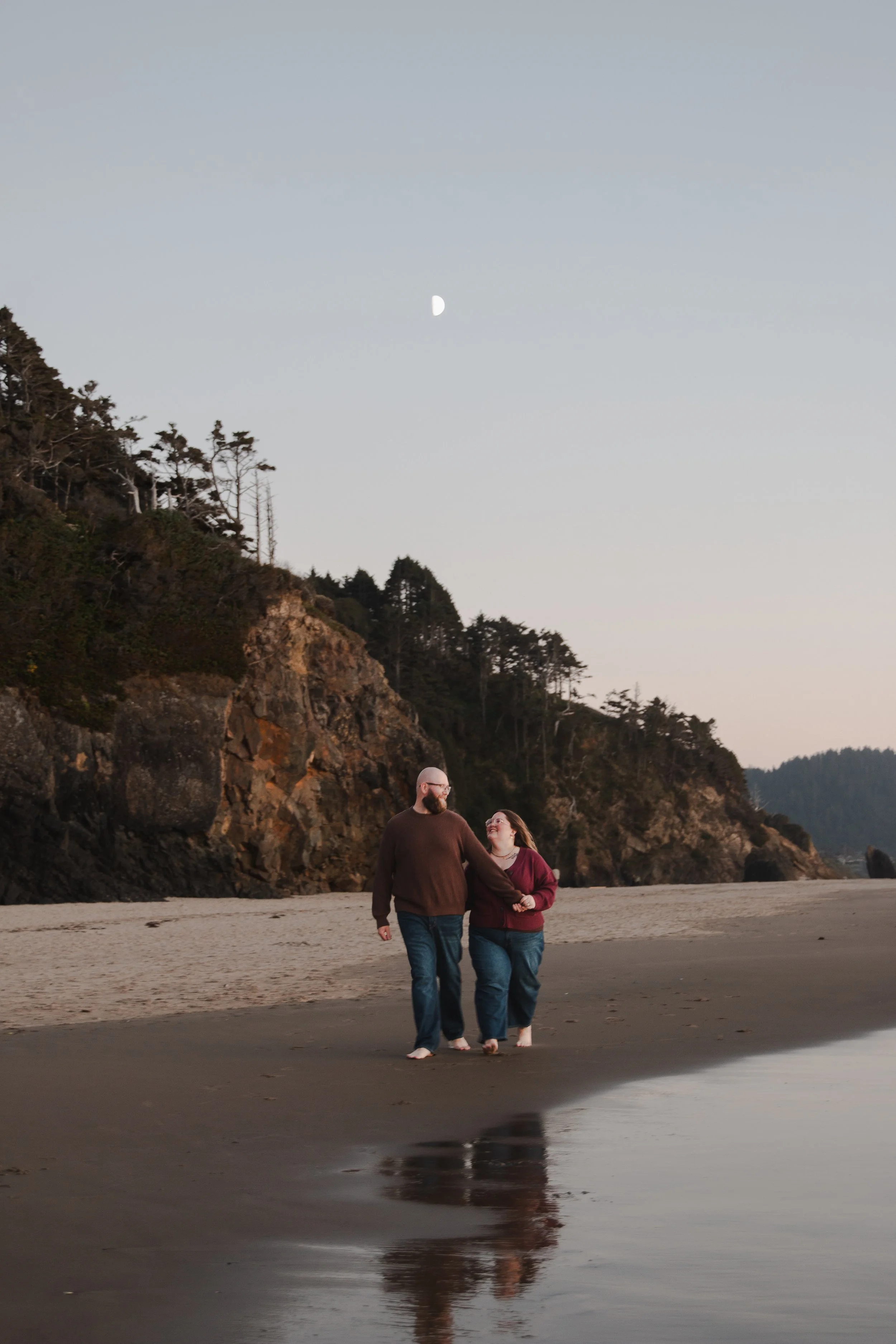Hug Point engagement session with couple walking beneath sandstone cliffs