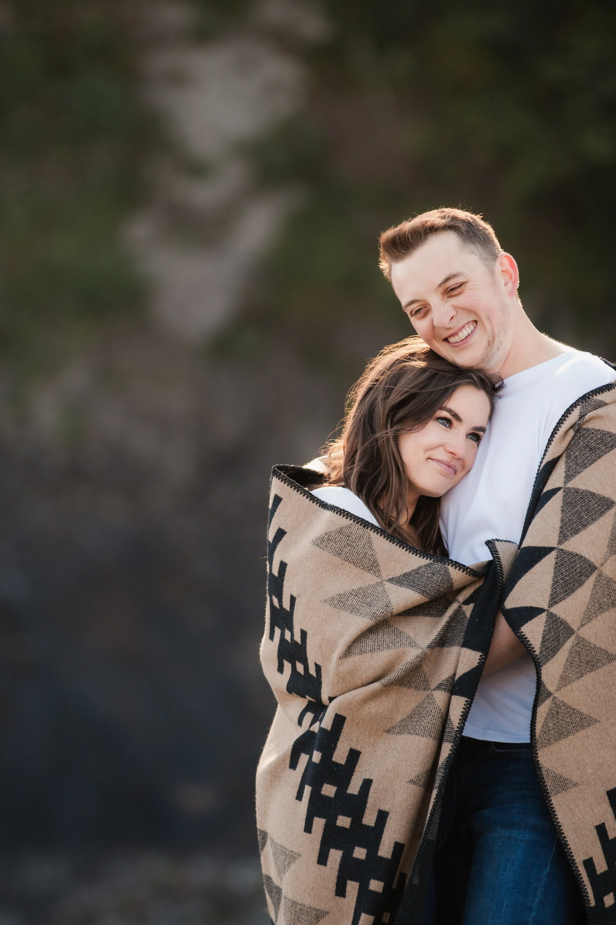 Engaged couple wrapped together in a Pendleton blanket during beach engagement photos on the Oregon Coast.
