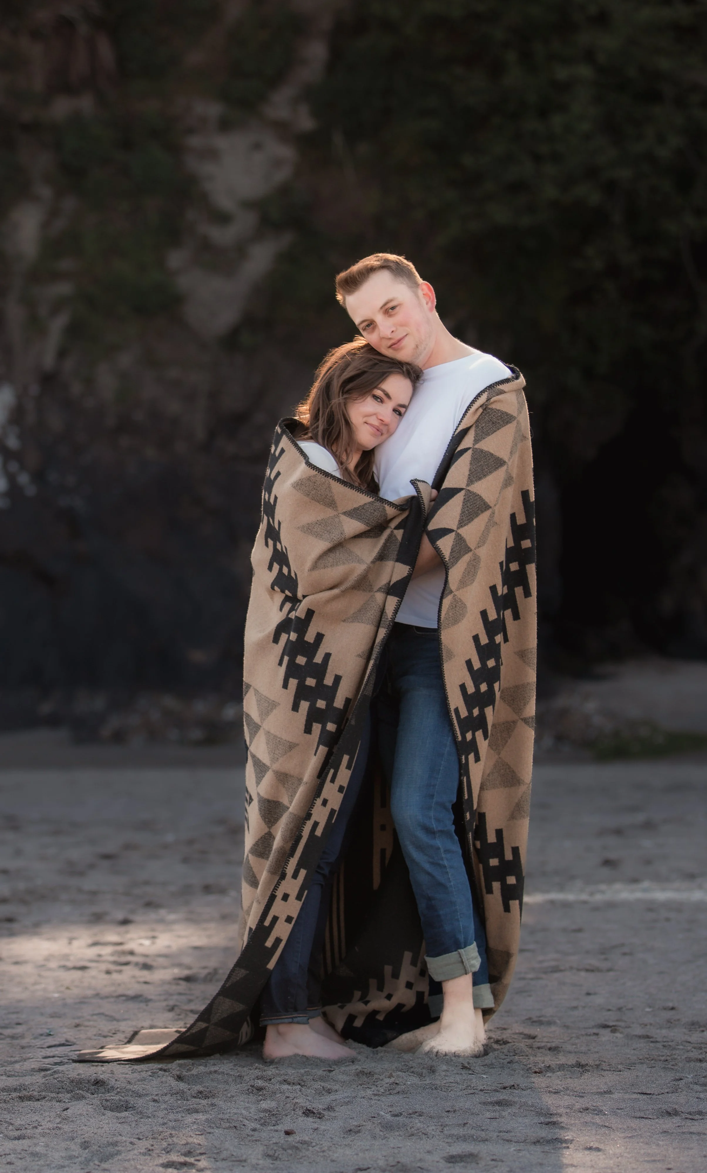 Engaged couple wrapped together in a Pendleton blanket during beach engagement photos on the Oregon Coast.