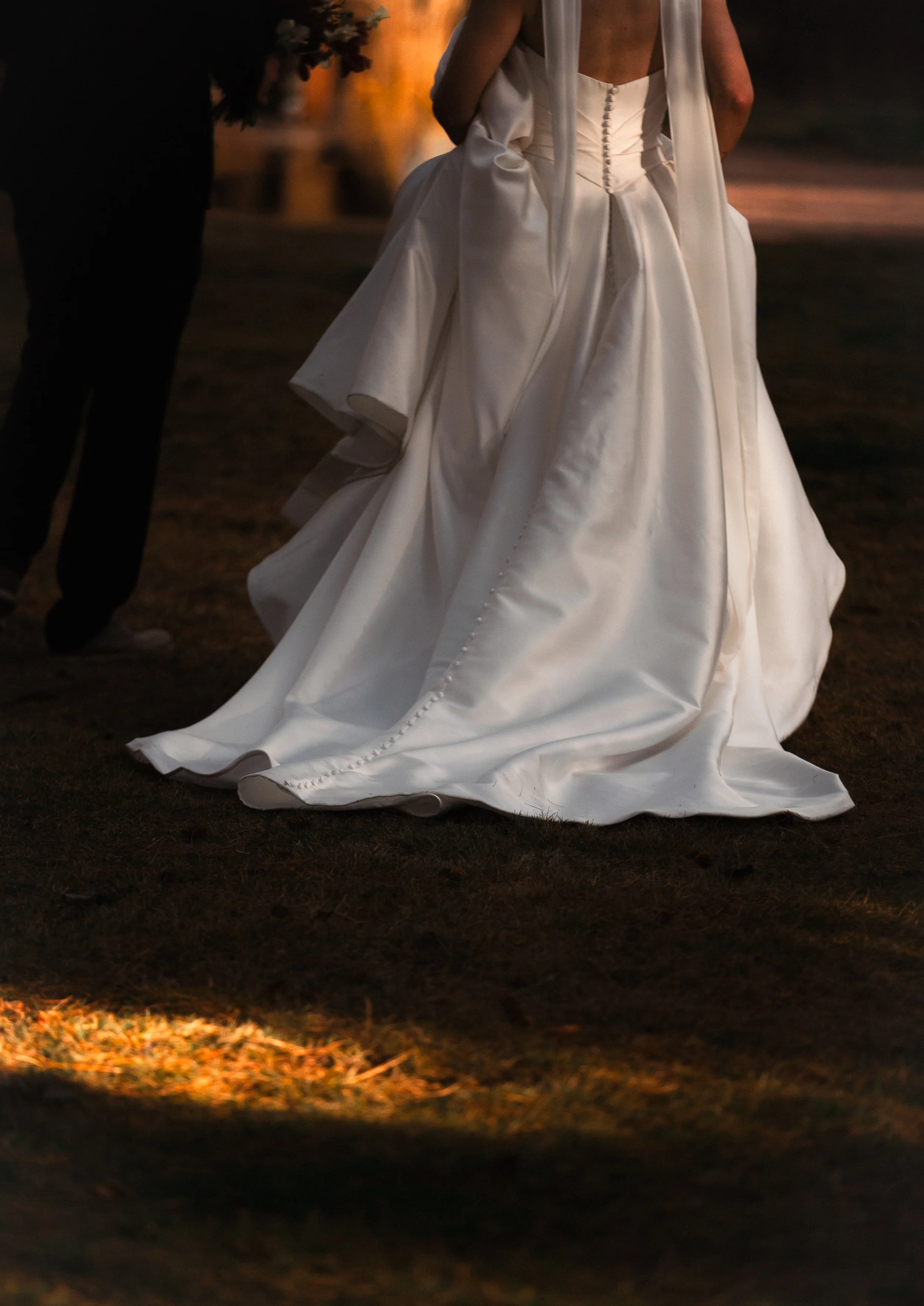 Editorial wedding detail of a bride's flowing satin gown in warm afternoon light.
