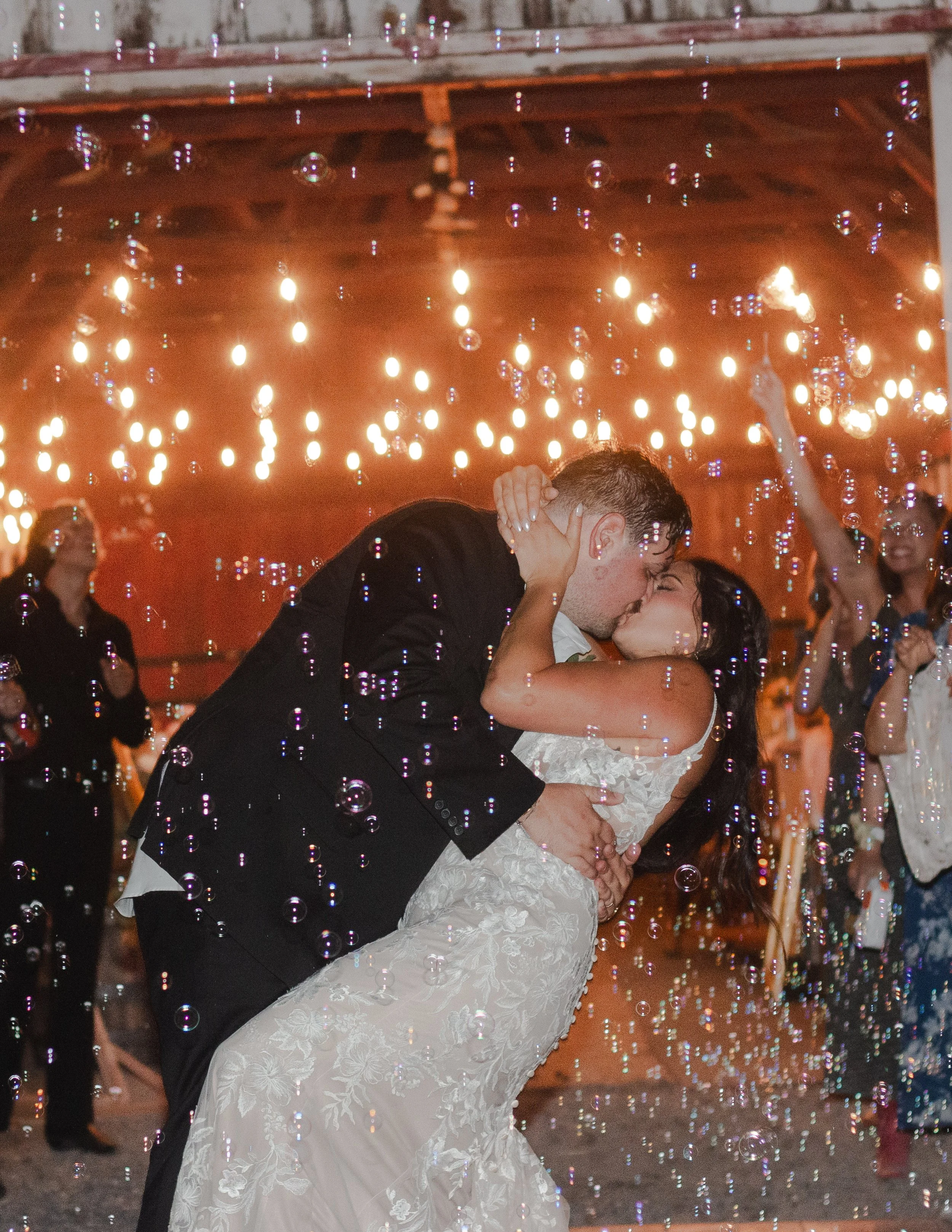 Newlyweds kissing beneath bubbles and string lights during their ranch wedding send-off.