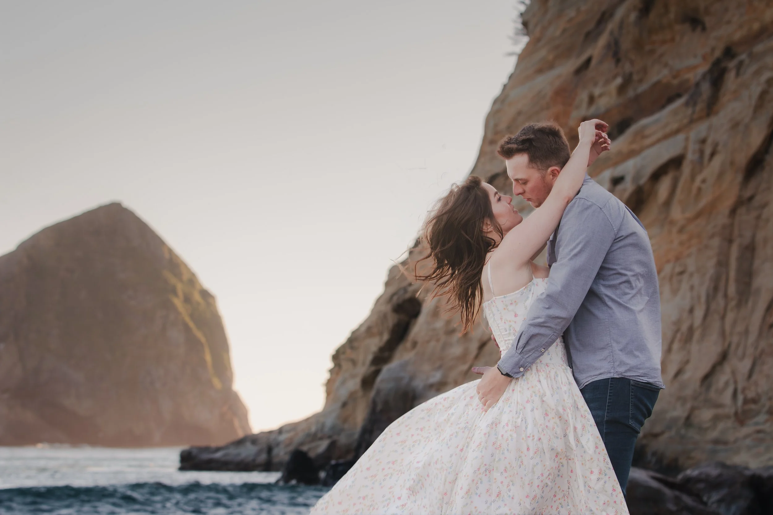 Engaged couple embracing on the beach beneath the cliffs near Cape Kiwanda, Oregon.