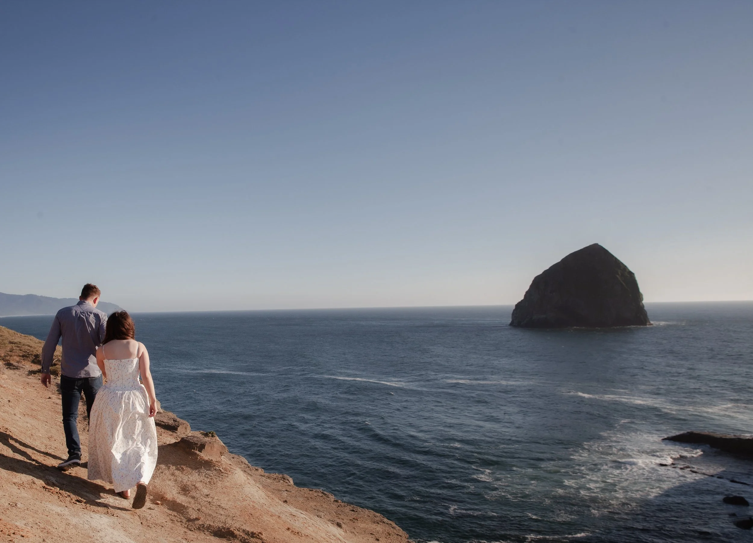 Engaged couple walking along the rocky coastline near Cape Kiwanda on the Oregon Coast.