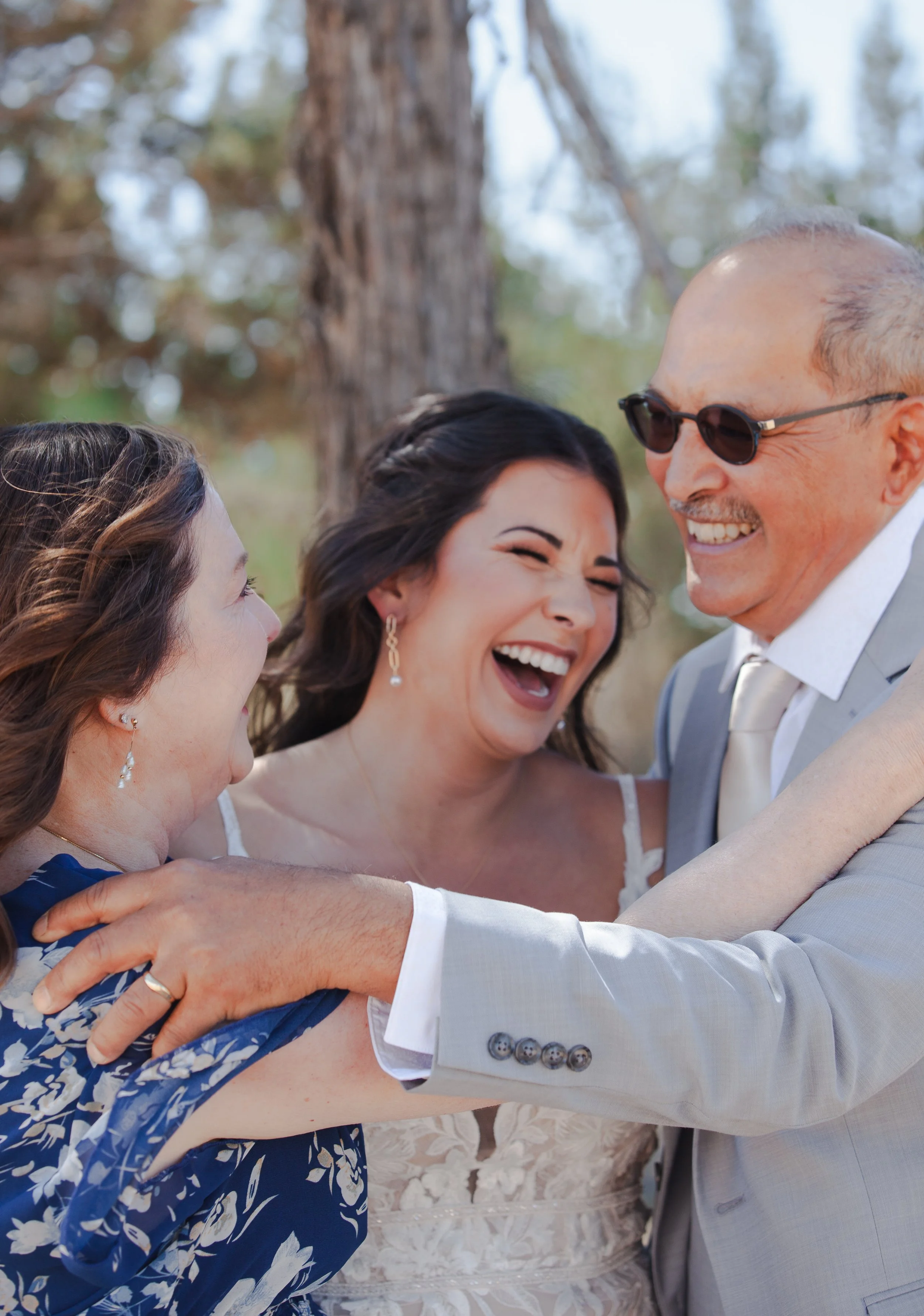 Bride laughing with her parents during a joyful family moment on her wedding day.