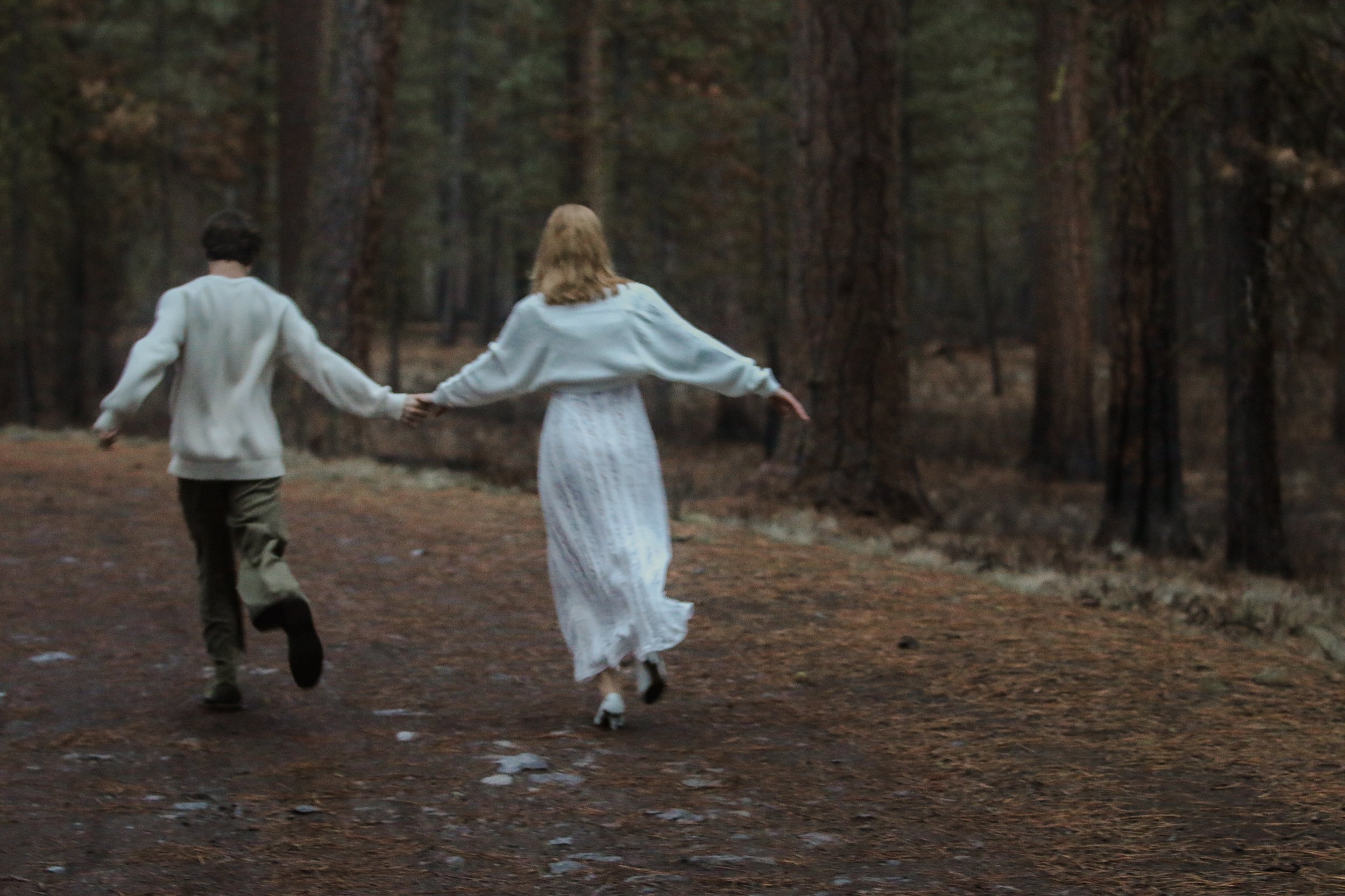 Candid engagement photo of a bride and groom running together through the Central Oregon woods.