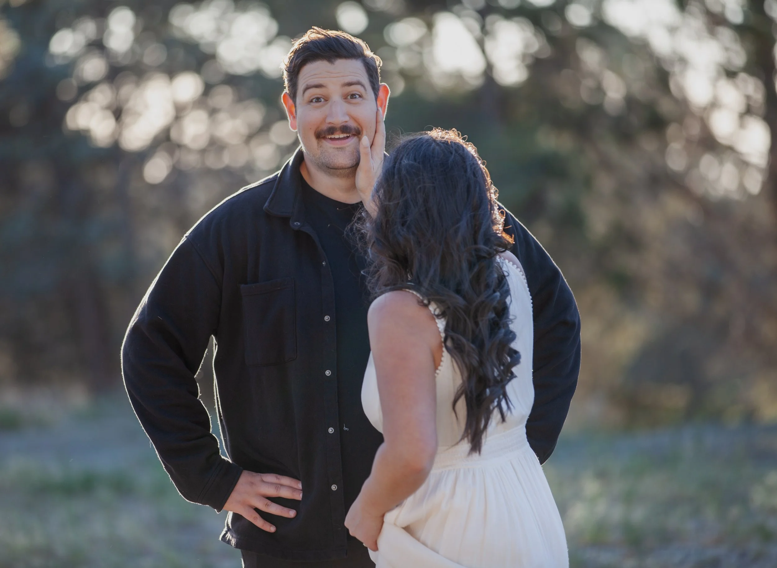 Playful Western engagement portrait of a couple laughing together beneath the pines near Bend, Oregon.