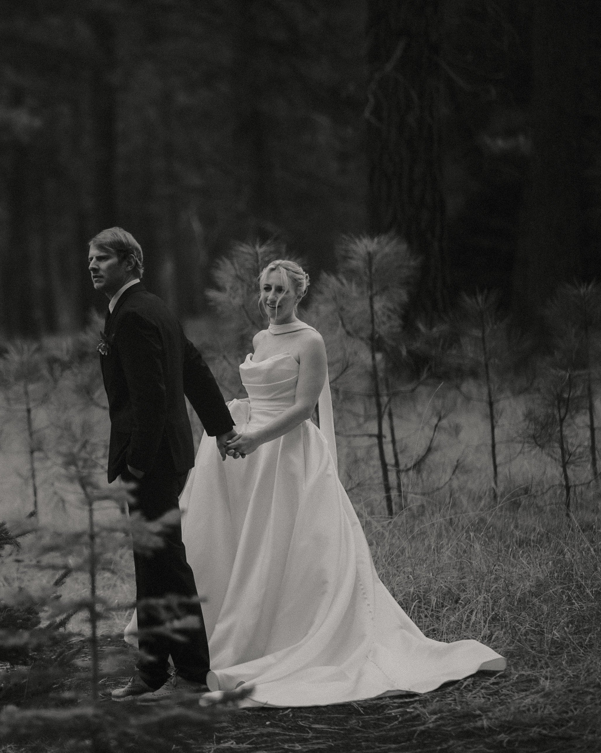 Black-and-white wedding portrait of a bride and groom walking through the Central Oregon pine forest.