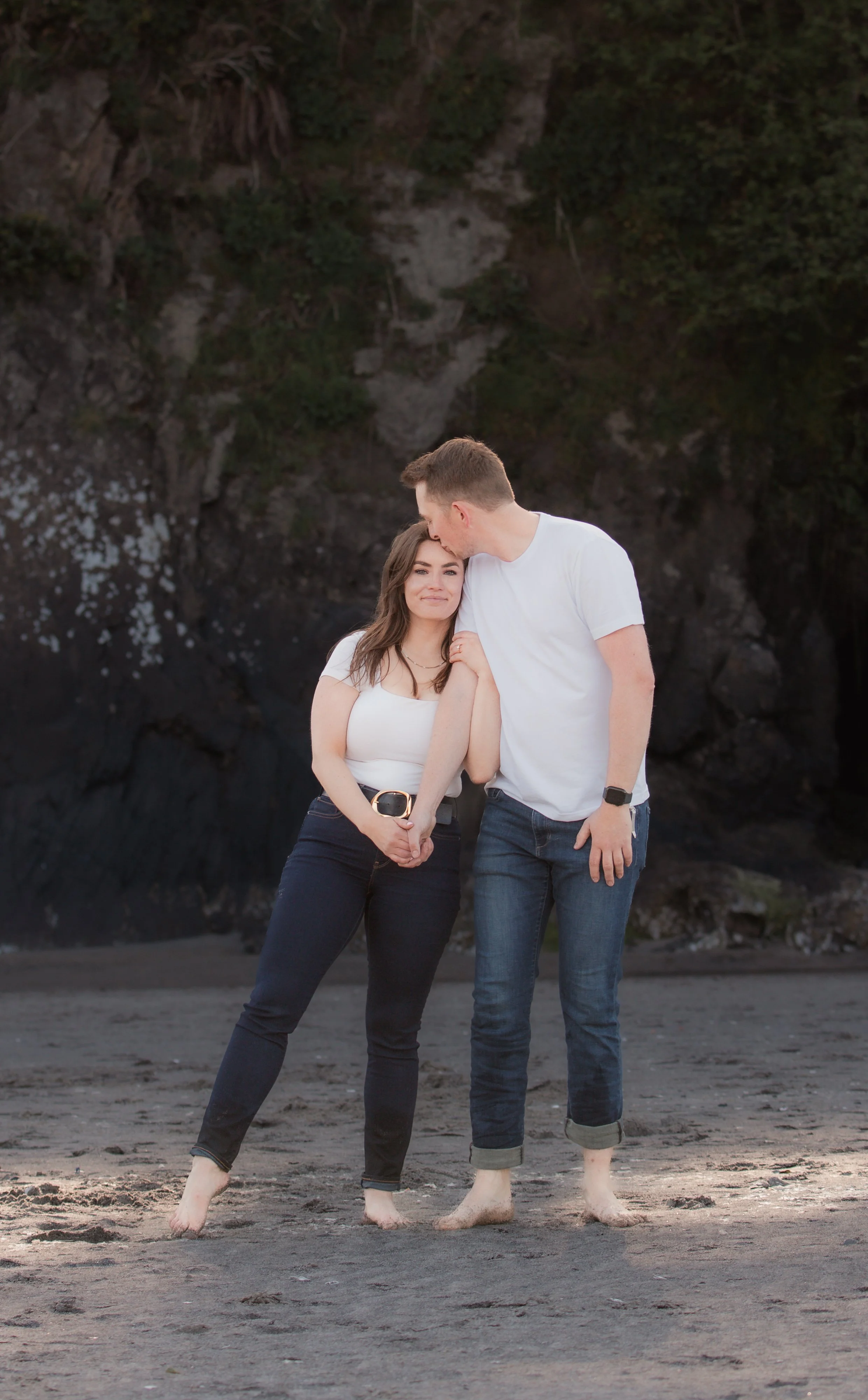 Bride and groom standing barefoot together beneath the coastal cliffs during their Oregon engagement photos.