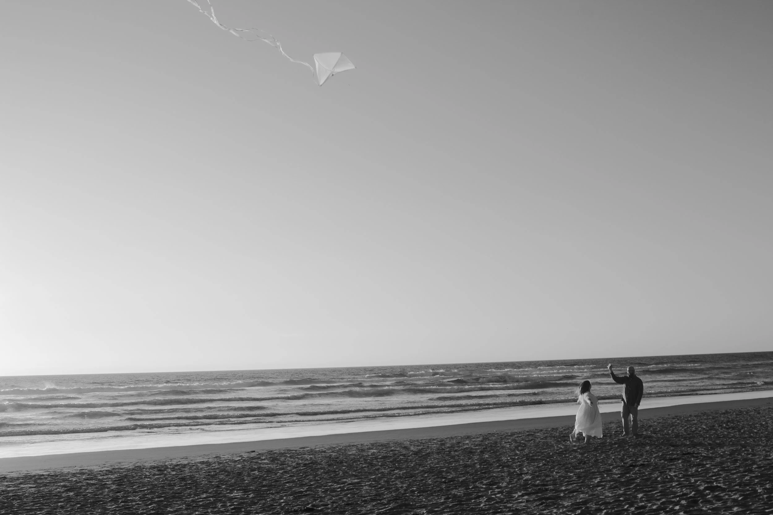 Cinematic beach engagement photo with couple and kite at sunset
