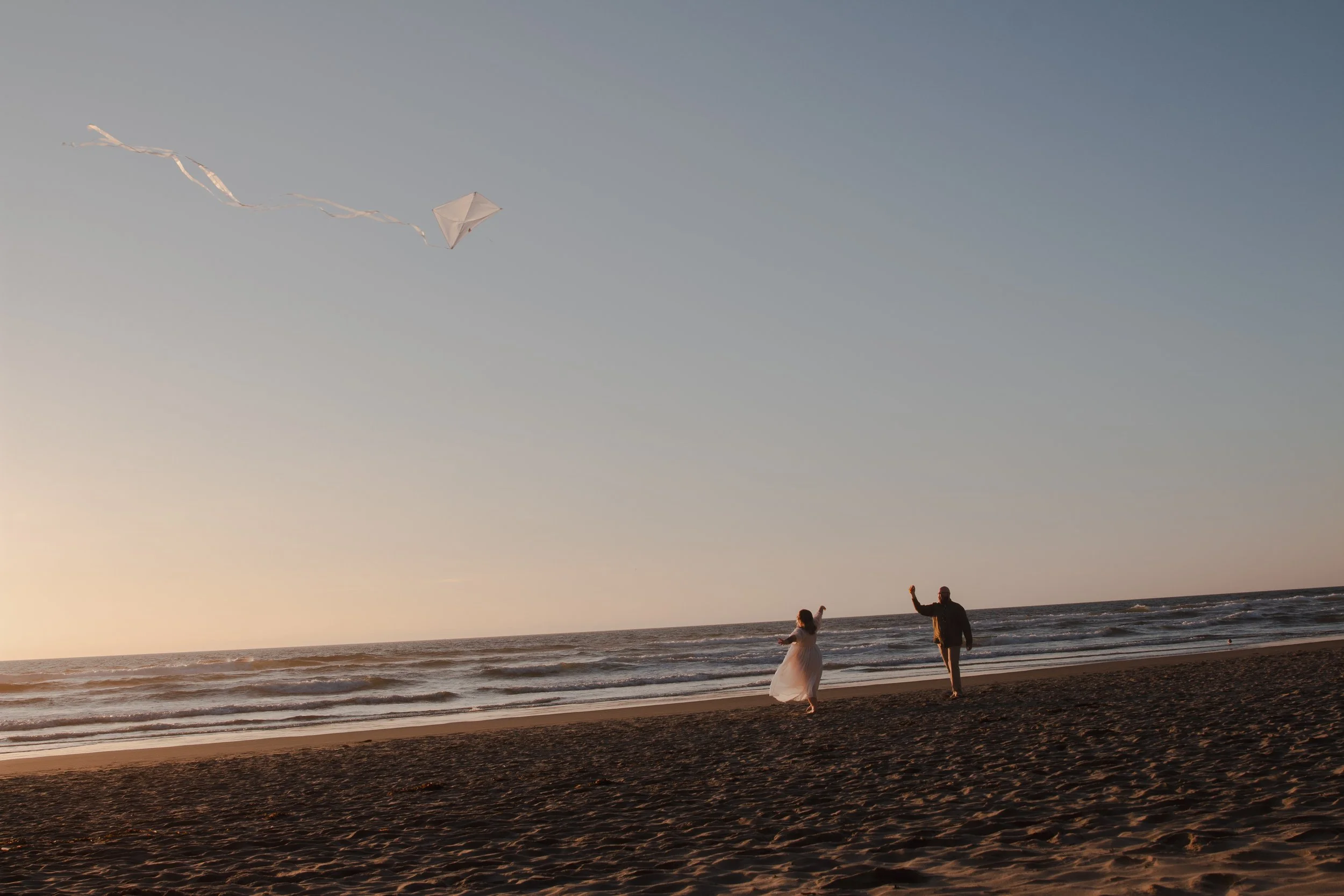 Bride-to-be dancing in the ocean while groom flies a kite at Hug Point