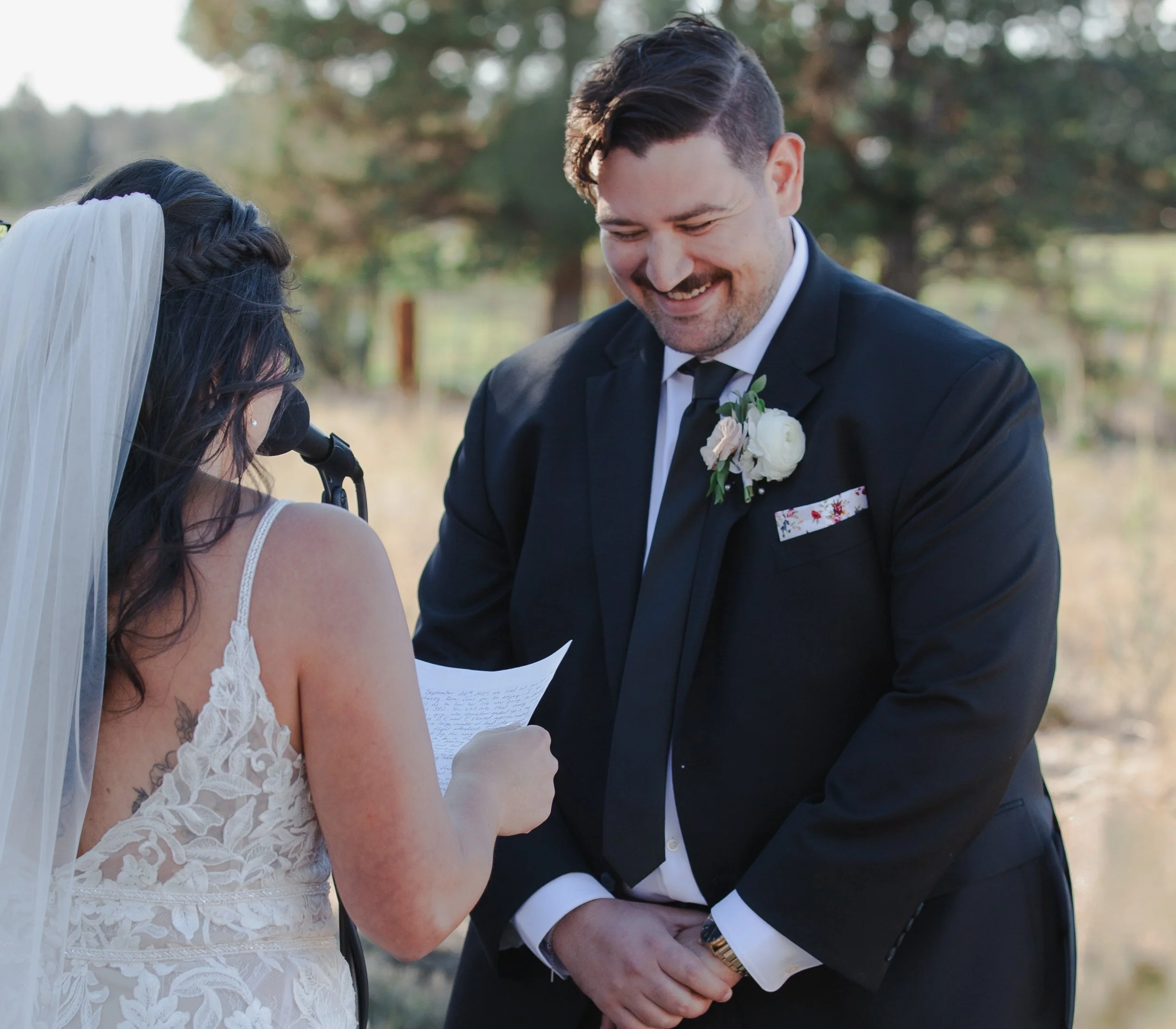 Groom smiling as his bride reads her vows during their outdoor Central Oregon wedding ceremony.