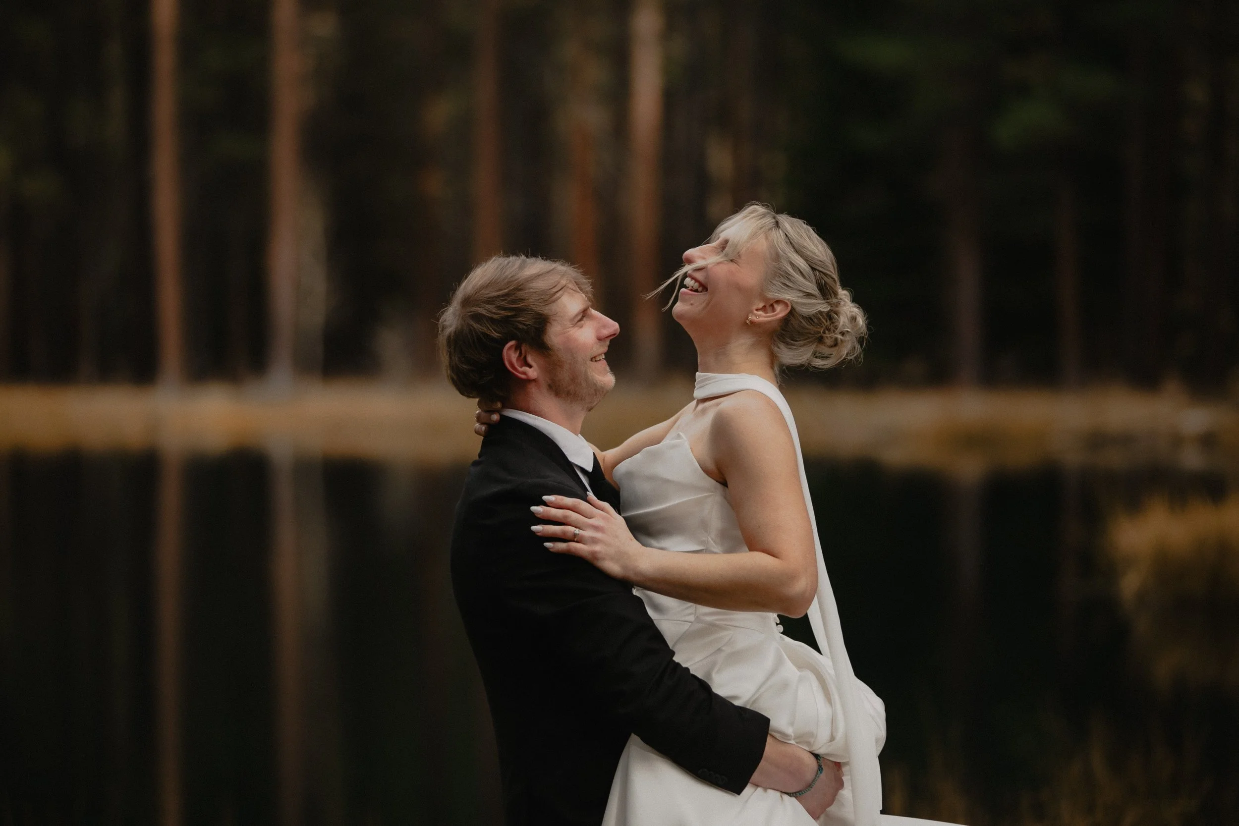 Romantic portrait of a groom lifting his bride beside the water at Lake Creek Lodge.