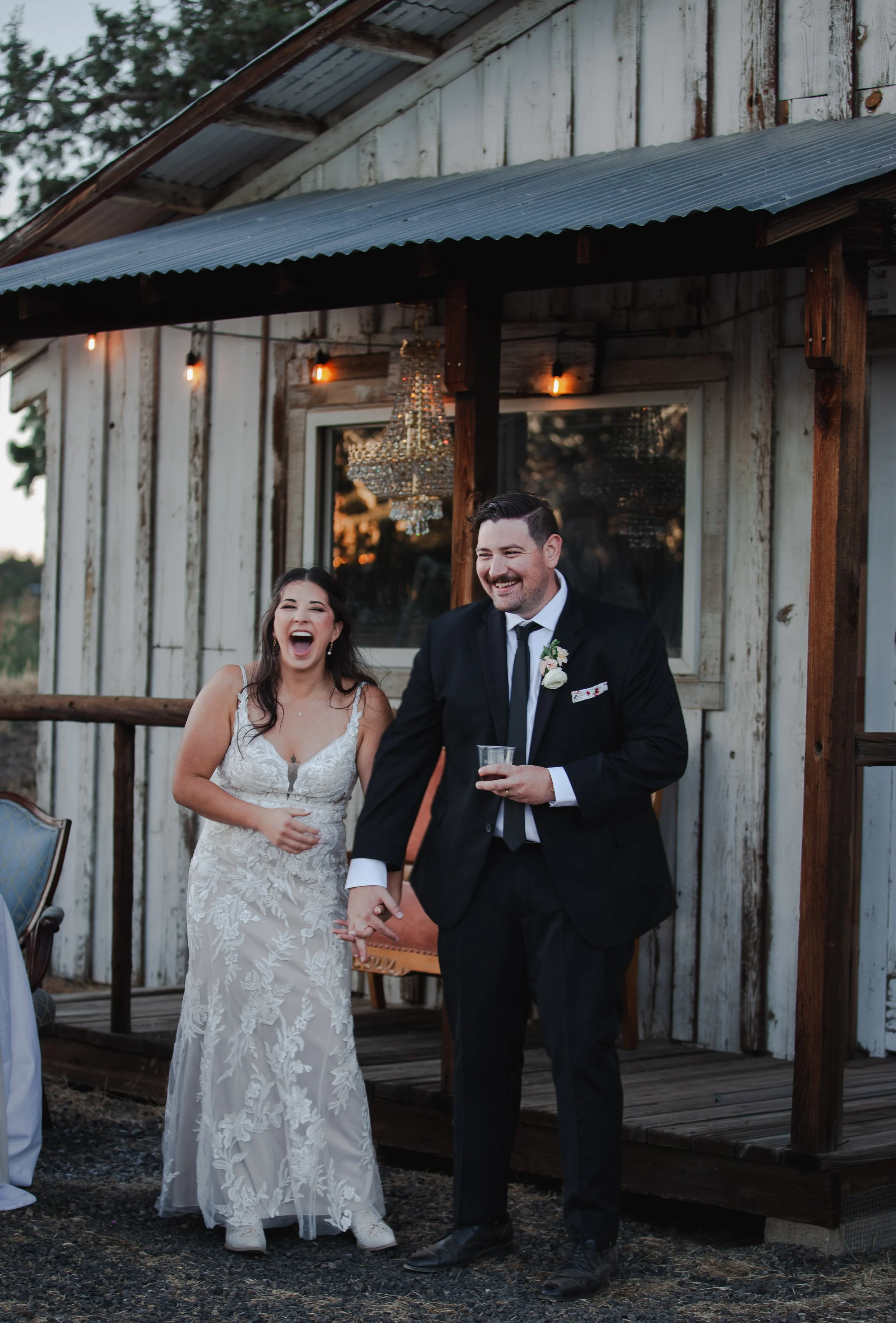 Bride and groom laughing together outside a rustic ranch building at their Central Oregon wedding.