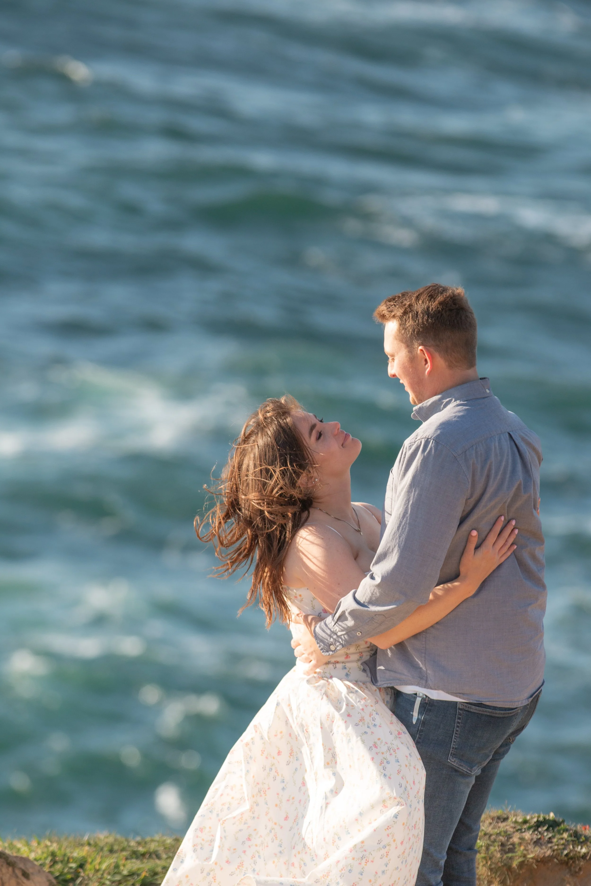 Couple embracing beneath dramatic coastal cliffs during an editorial engagement session. Oregon Coast.